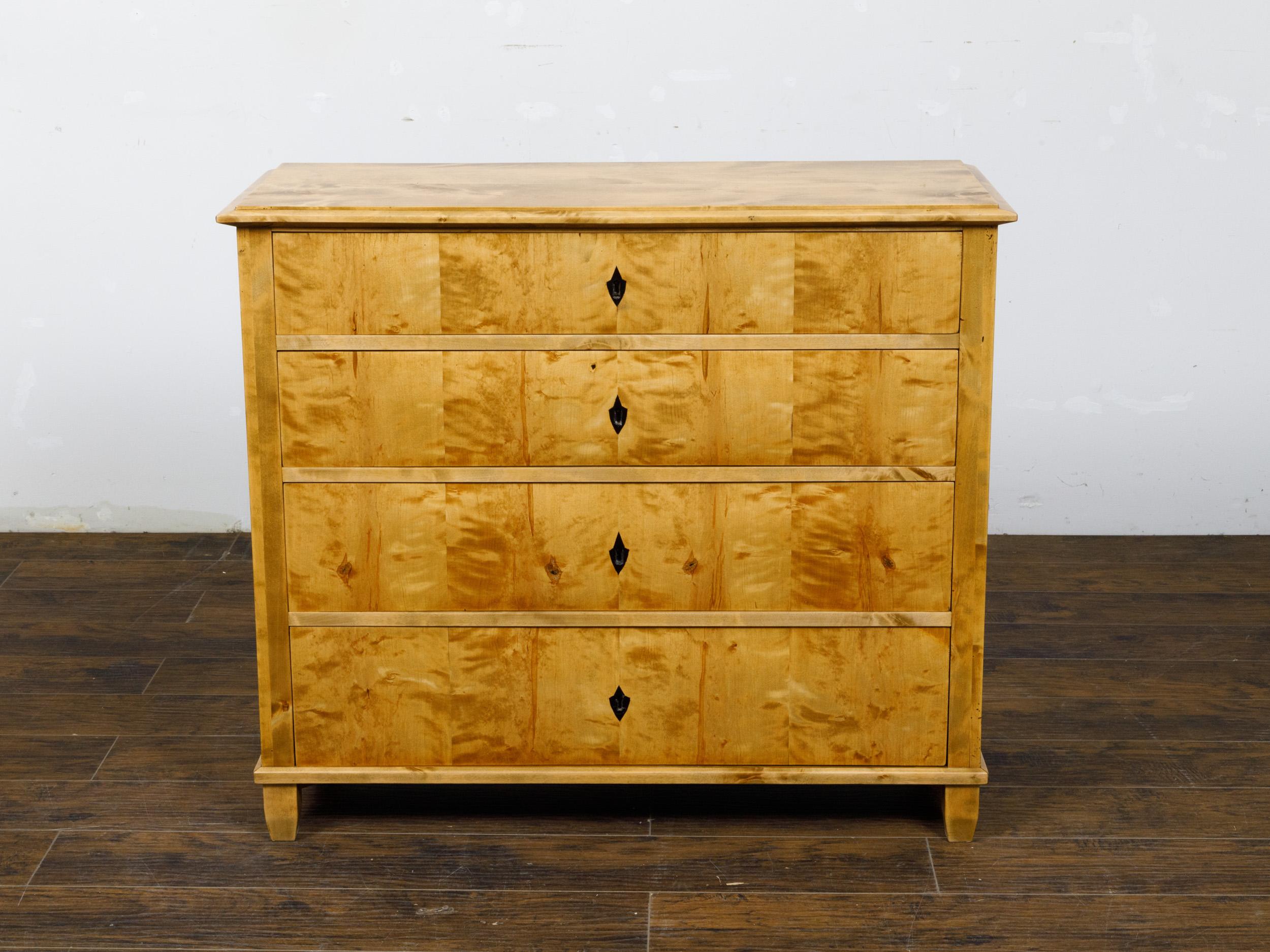 A Biedermeier period maple wood four-drawer chest from the 19th century with inlaid escutcheons. This Biedermeier maple wood four-drawer chest from the 19th century epitomizes timeless elegance and masterful craftsmanship. The chest features a warm,
