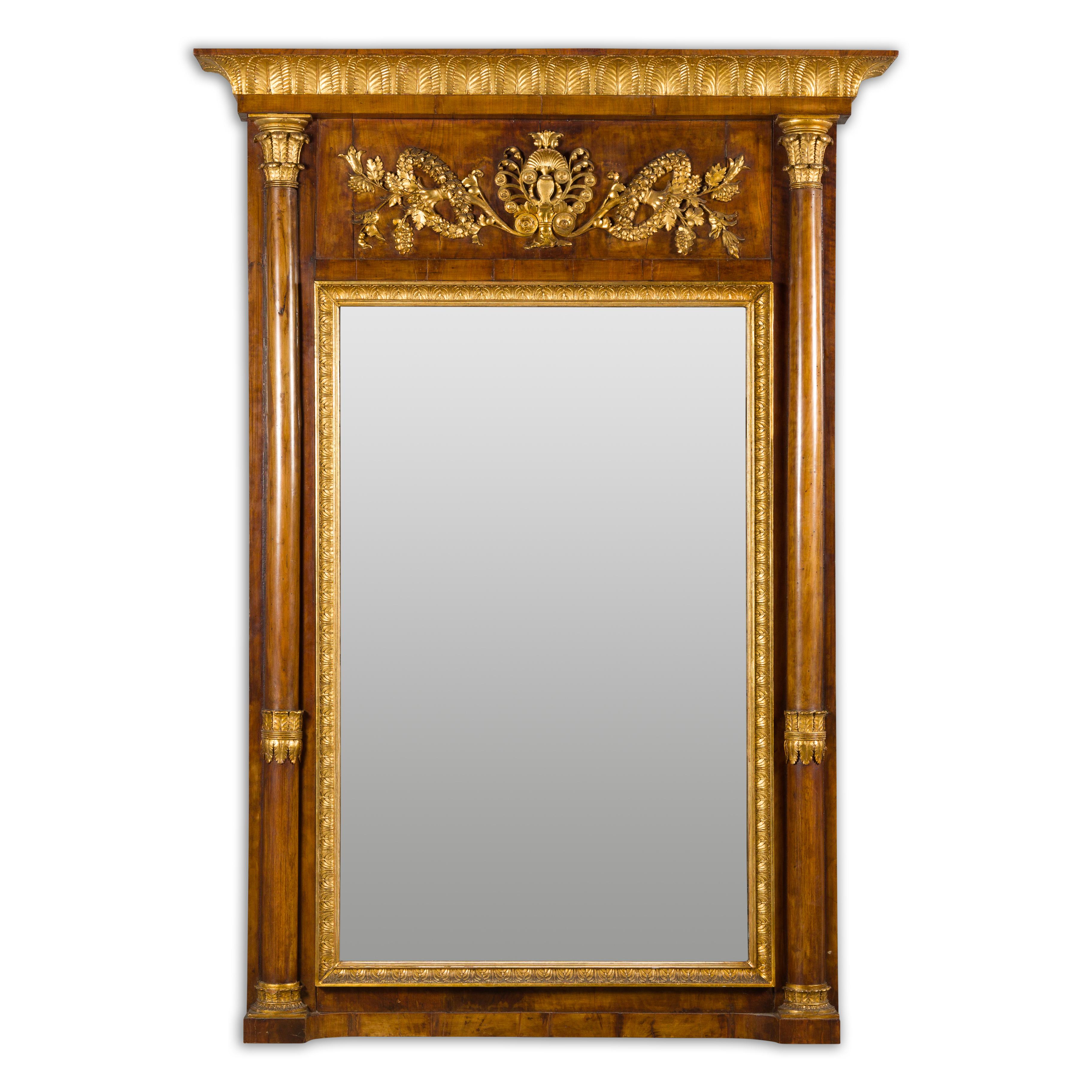 An Austrian Biedermeier period walnut tall pier mirror from the 19th century, with carved giltwood foliage, slender columns and frieze of palmette motifs. This Austrian Biedermeier period walnut tall pier mirror from the 19th century is an exquisite