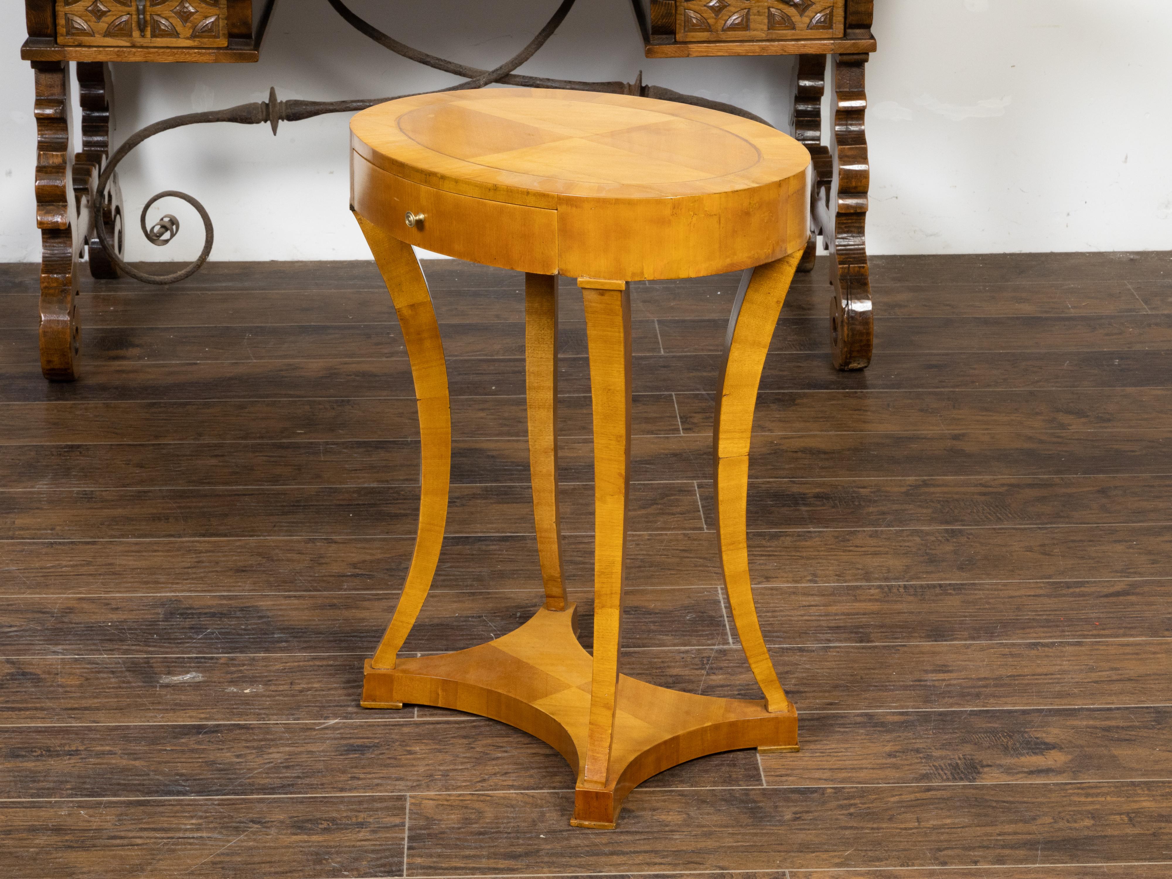 An Austrian Biedermeier period walnut accent table from the 19th century, with oval top, quarter veneer, banding, single drawer, saber legs and low in-curving stretcher. Created in Austria during the Biedermeier period in the first half of the 19th