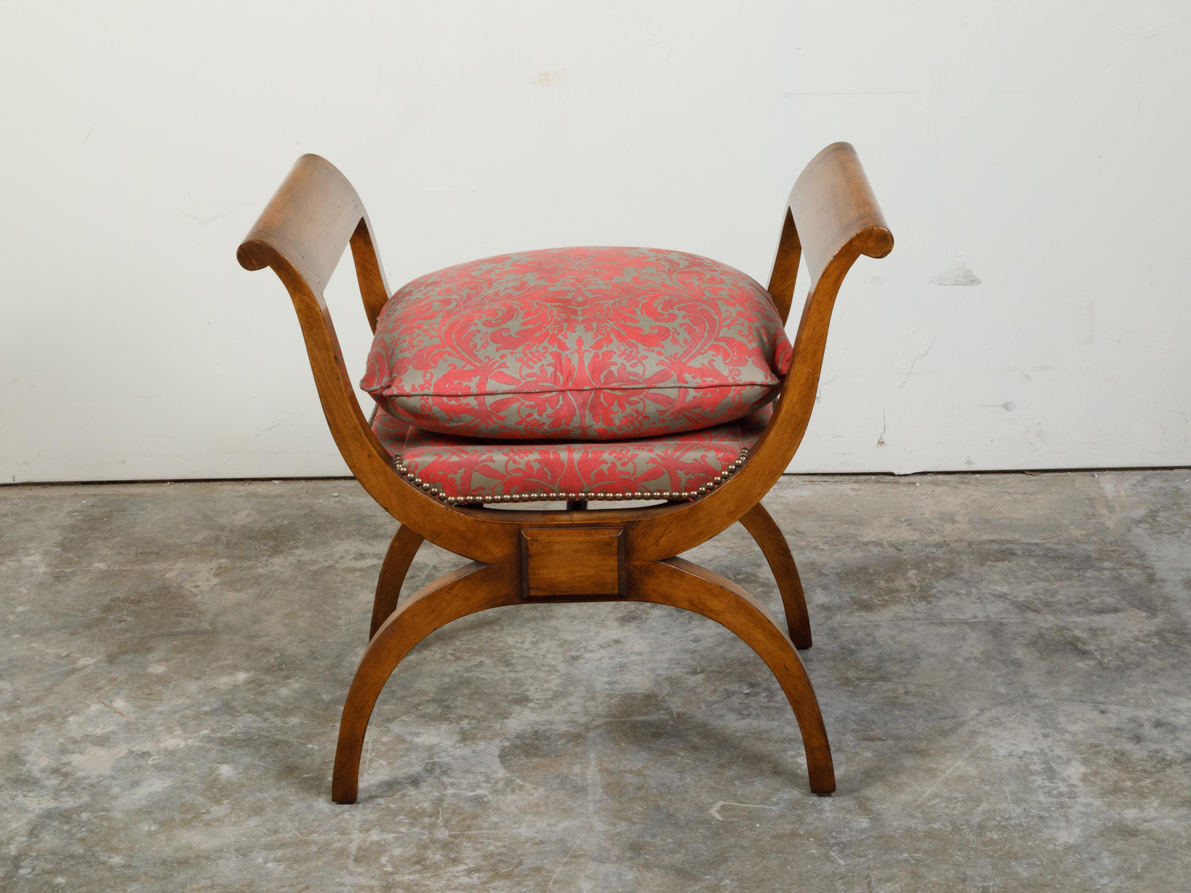 An Austrian Biedermeier period X-form walnut stool from the 19th century, with out-scrolling arms and upholstery. Created in Austria during the 19th century, this Biedermeier walnut stool features two out-scrolling arms flanking an upholstered seat