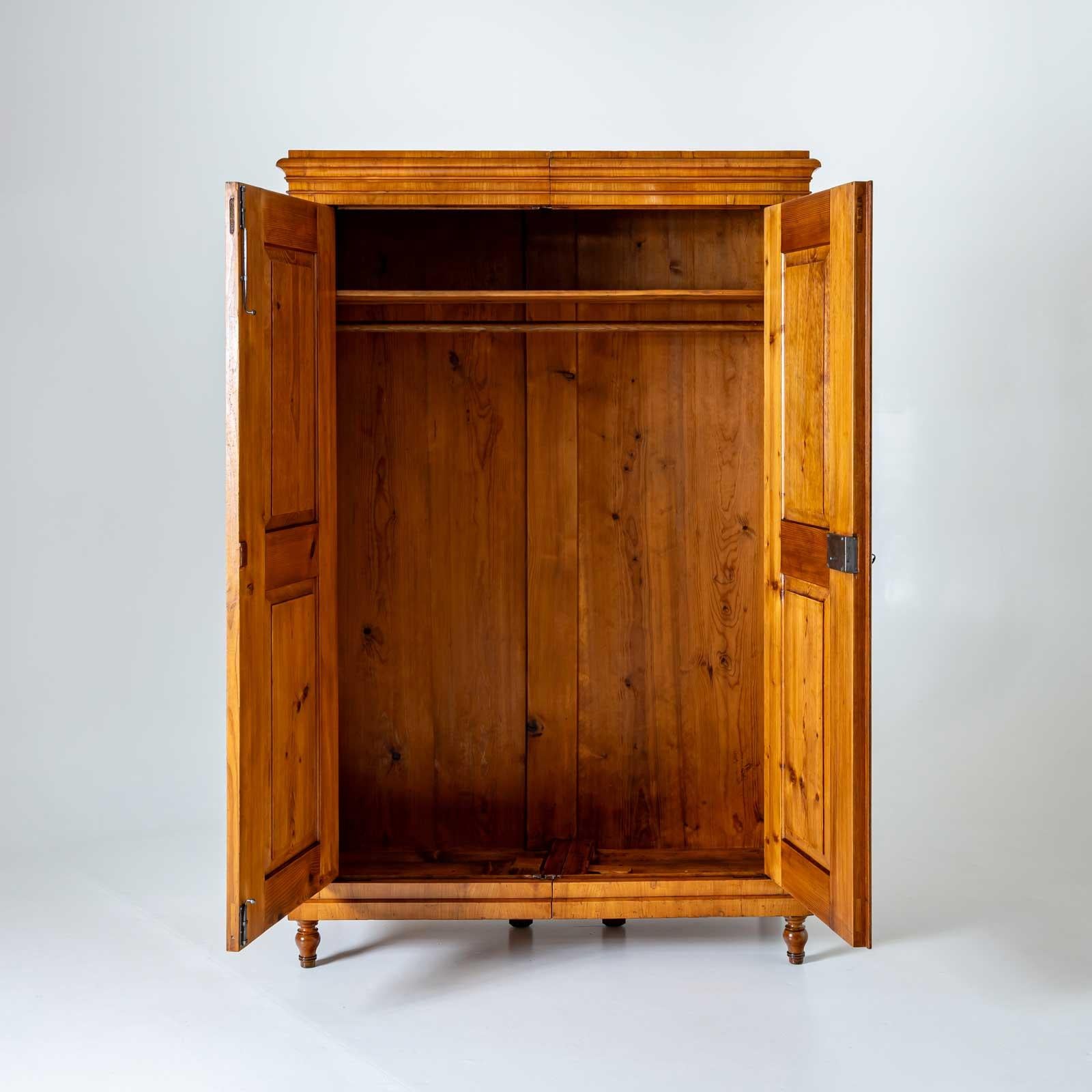 Mobile Biedermeier a due ante in ciliegio con campi pannellati sulle ante e gambe a balaustro. La cornice è modellata più volte. L'armadio è dotato di un ripiano e di un appendiabiti.