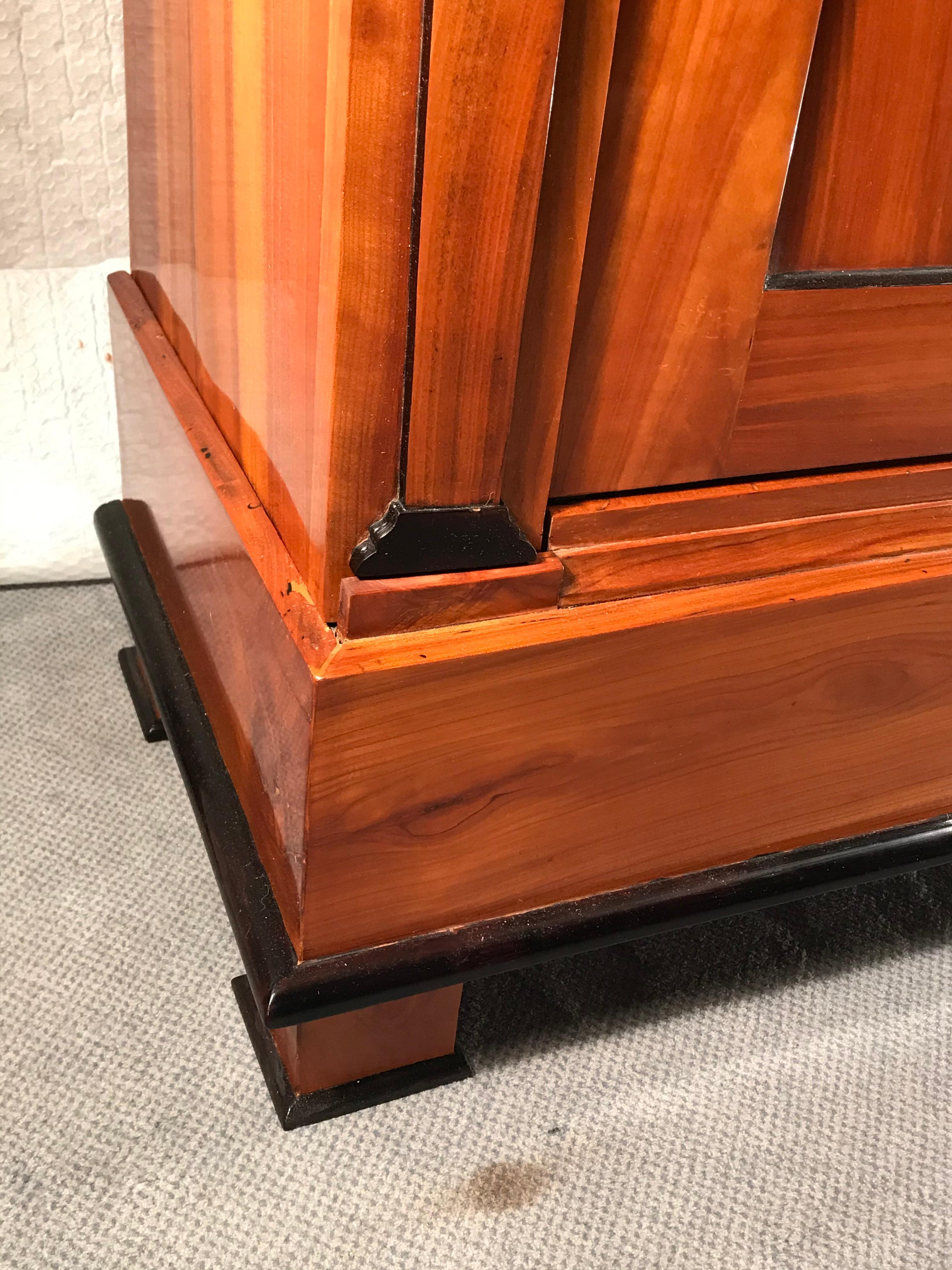 Beautiful original Biedermeier Armoire, South German 1810-1820, mirrored cherry wood veneer with ebonized details. The interior has three original shelves and two drawers. The armoire is refinished and French polished. It ships from Germany.