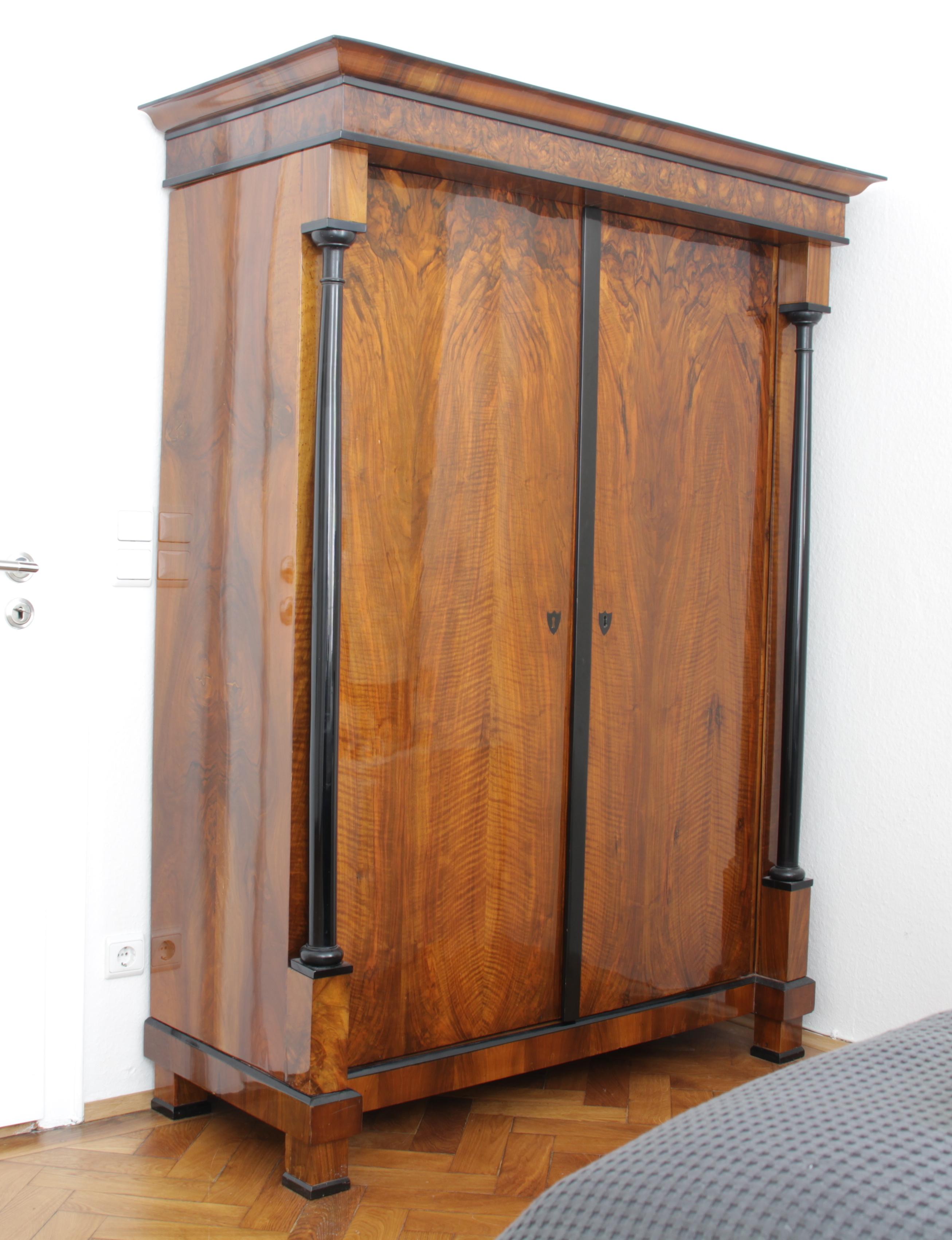 Straightlined, unadorned early Biedermeier Armoire from Austria, circa 1820.
This two-door neoclassical armoire or wardrobe has a beautifully selected, book-matched walnut veneer and ebonized full columns with carved capitals and bases.
It has been