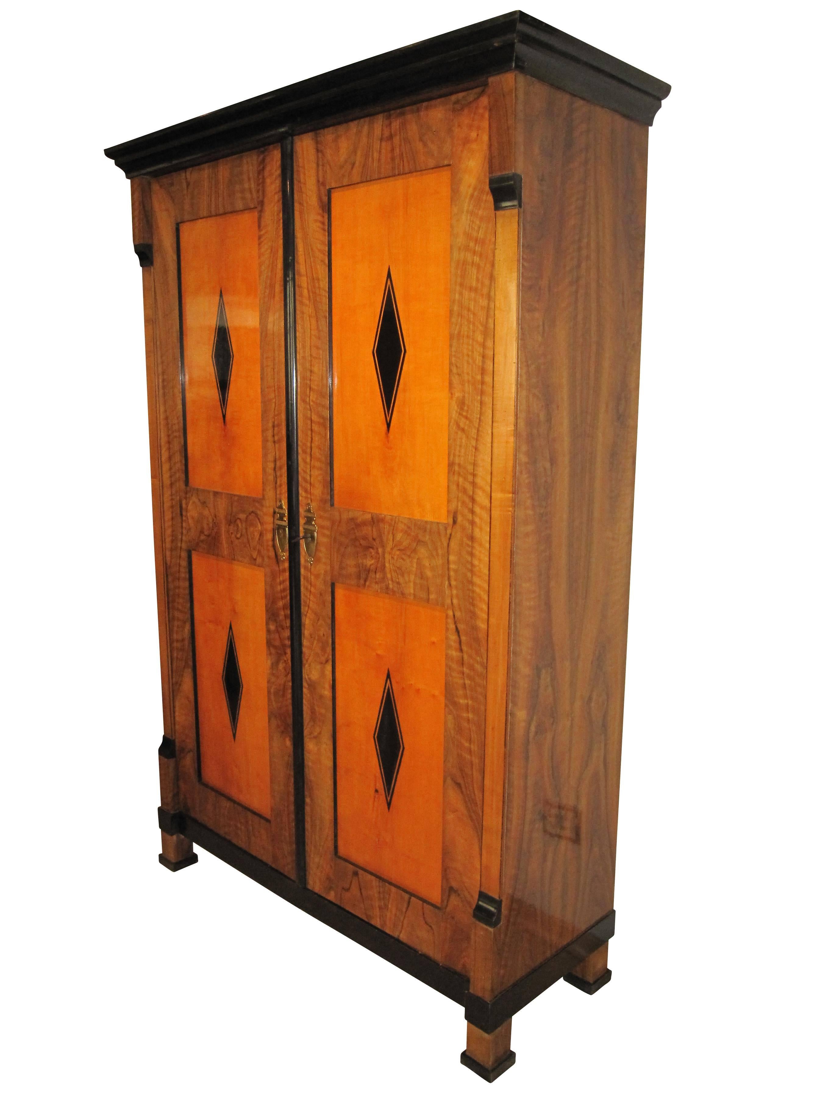 This two-doored early Biedermeier armoire is from Vienna, Austria, built around 1820. It has four maple fillings inside the walnut veneered framed boxes. On each of the fillings there is a typical classicist hash carefully with painted with Ink. the