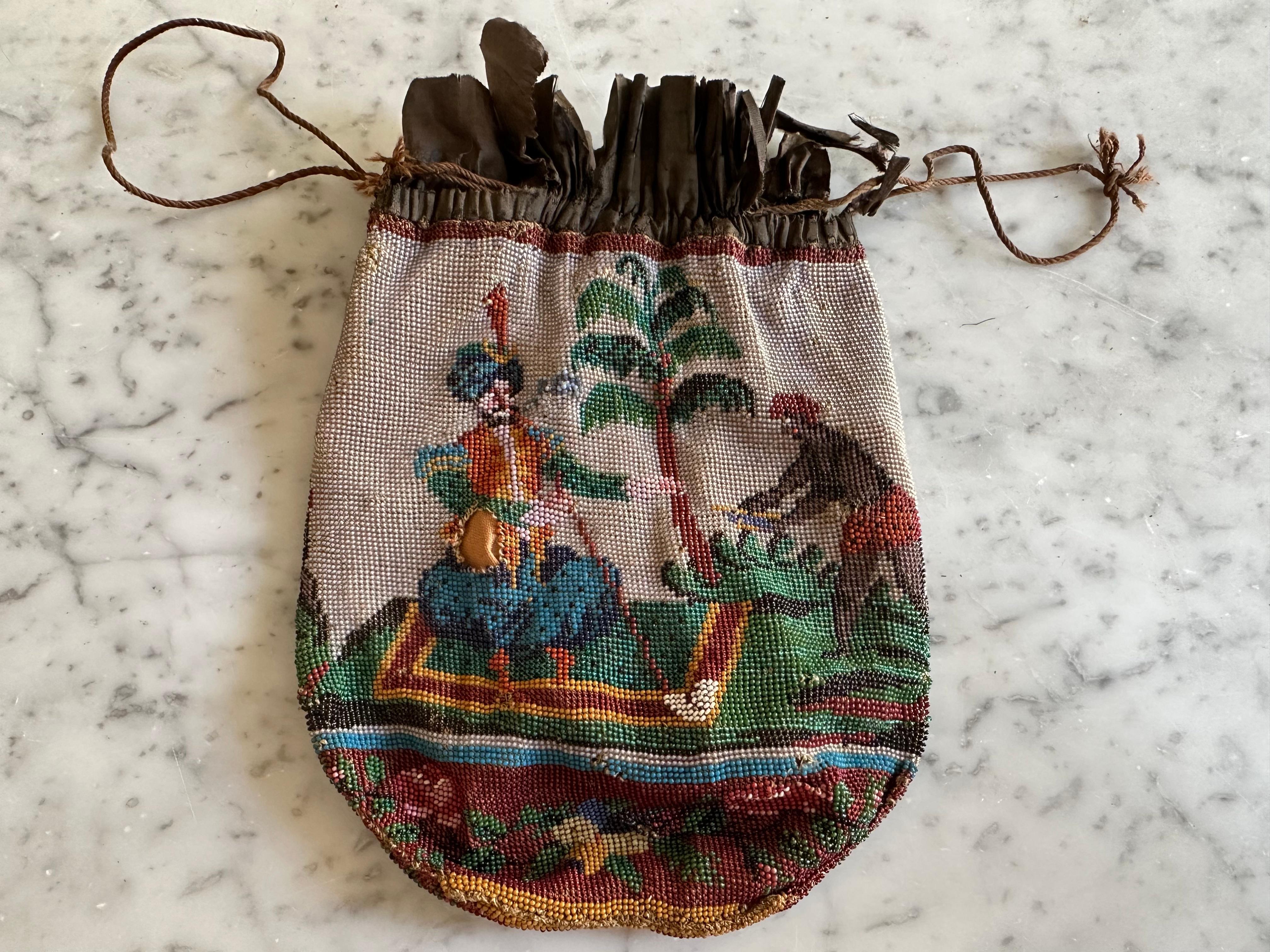 Ce rare sac en perles Biedermeier du XIXe siècle est un bel exemple de perlage européen ancien, à la fois décoratif et riche en détails narratifs. Le sac rond présente des deux côtés une scène élaborée, cousue à la main, entièrement réalisée avec de
