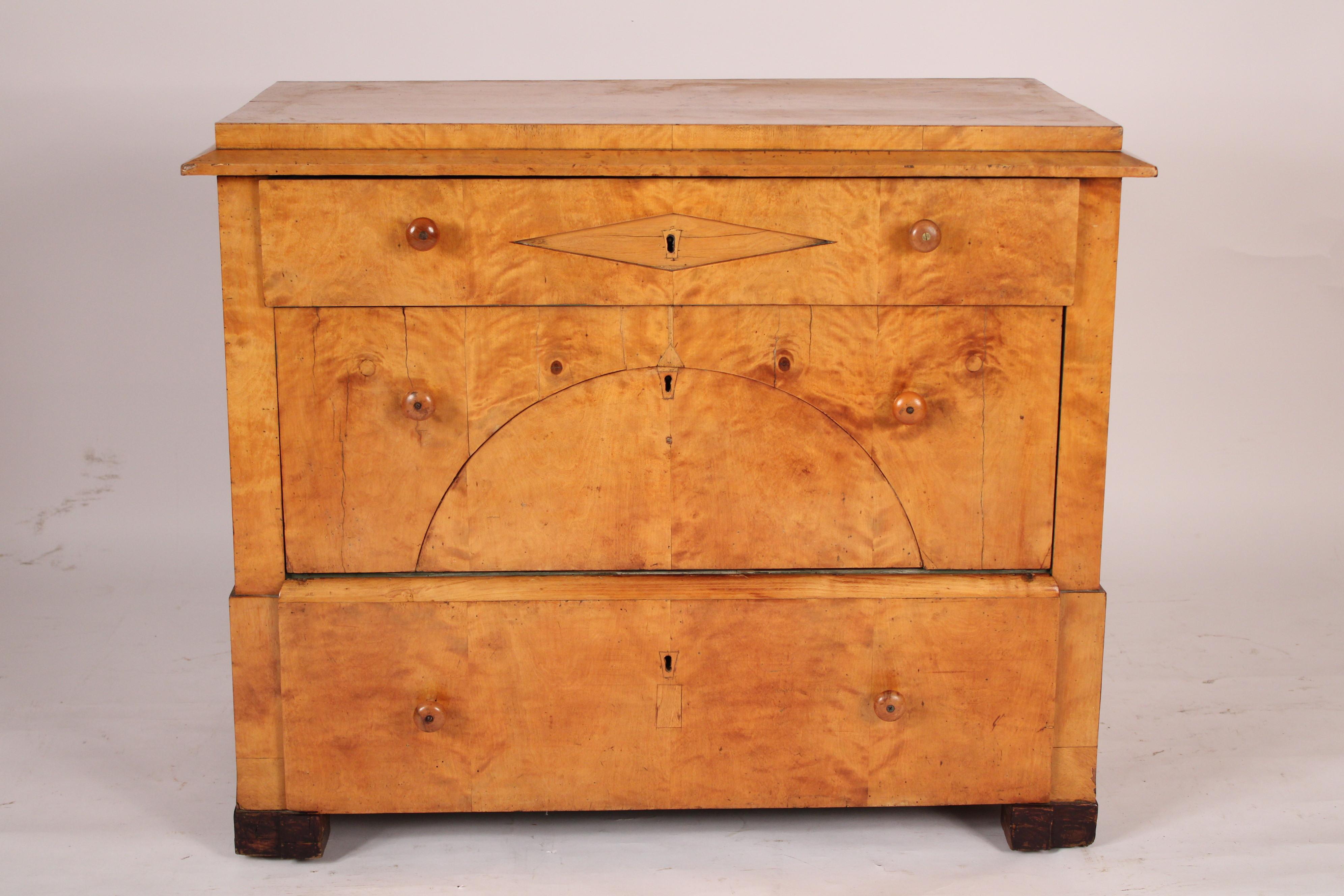 Biedermeier birch 3 drawer chest of drawers, 19th century. With a rectangular top a top drawer with central diamond shape inlay, middle drawer with a semi circular arch and a bottom drawer. Resting on later black ebonized feet.
