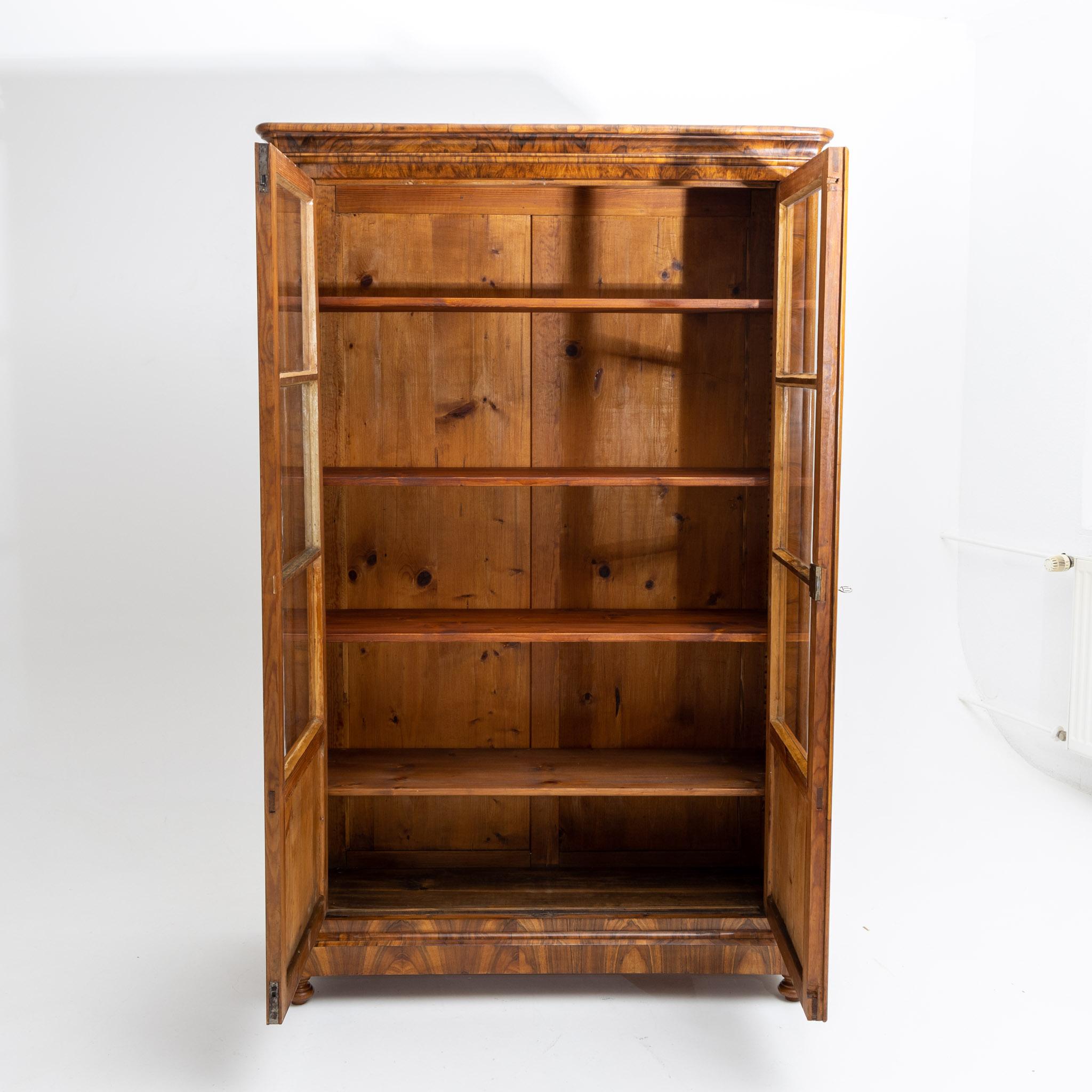 Two-door Biedermeier bookcase veneered in walnut, with three-quarter glazing and profiled cornice and small baluster feet in front and square feet in the back. Interior partition consists of movable shelves. Restored and hand polished condition.