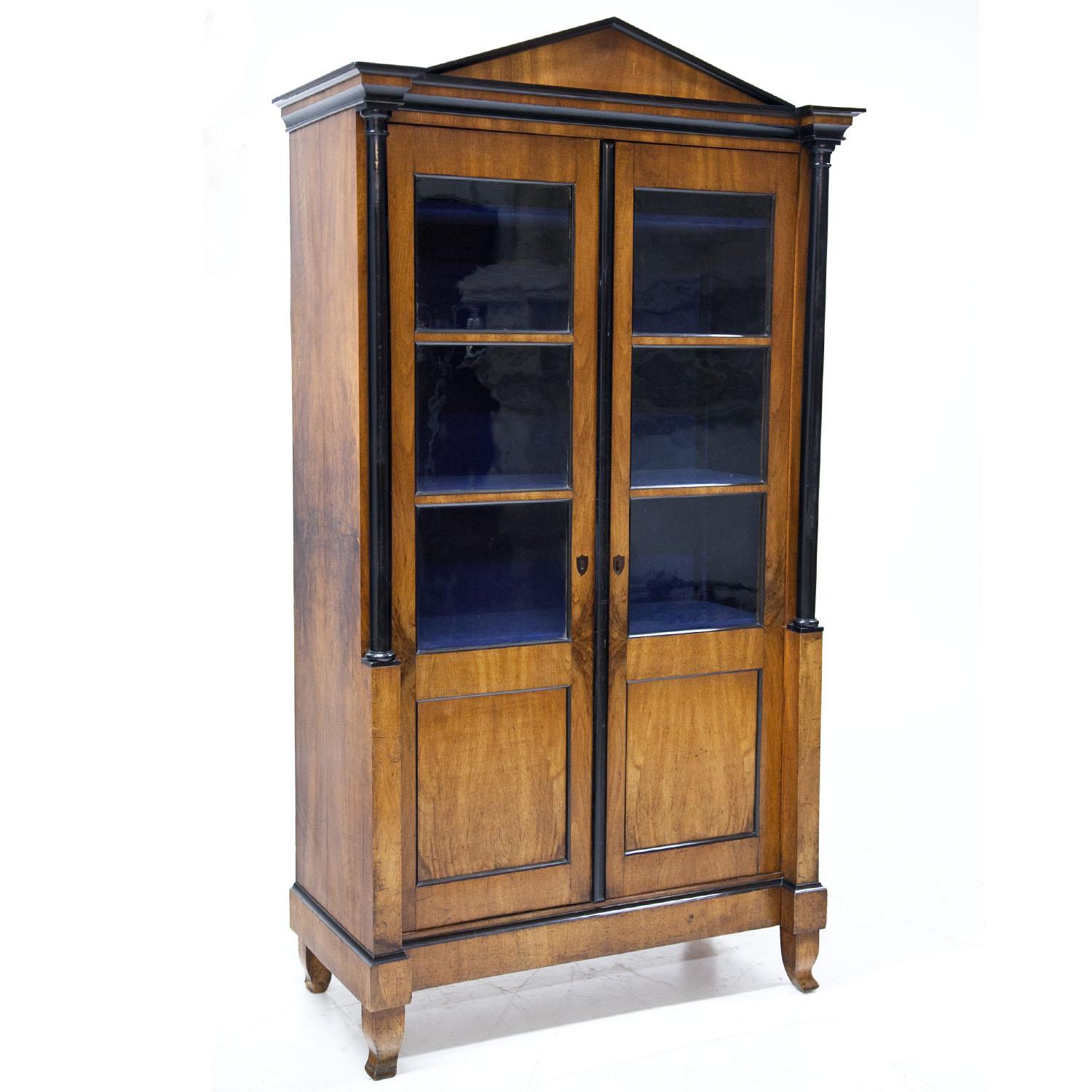 Two-doored walnut Biedermeier bookcase with an angular pediment with ebonized moldings as well as ebonized columns. The doors show three-quarter glazing and have fillings with ebonized moldings.