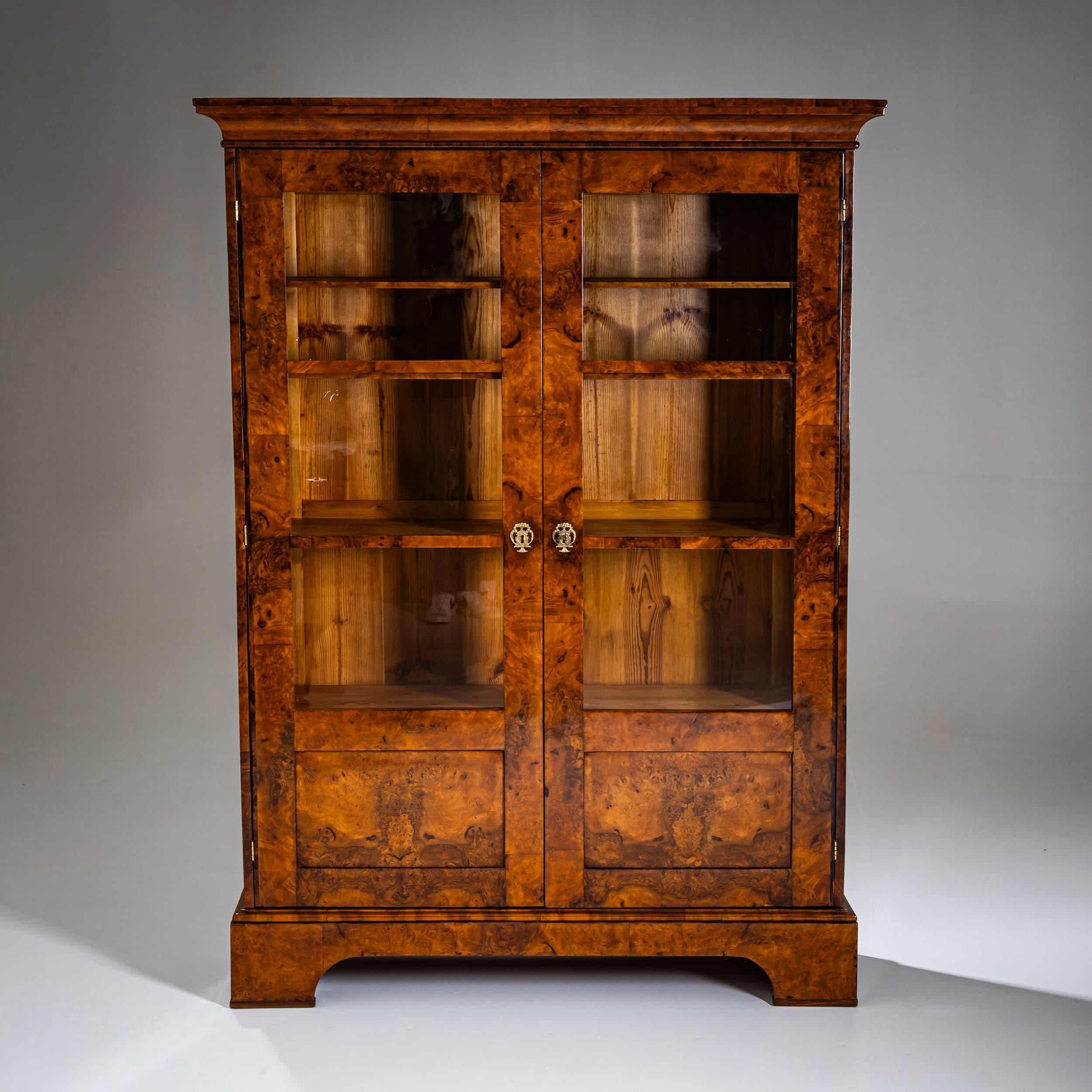 Bibliothèque Biedermeier à deux portes avec vitrage trois-quarts. La pièce repose sur une base en forme de tablier et est plaquée de ronce de noyer magnifiquement figurée. Les écussons sont en bronze doré au feu. L'intérieur est équipé de quatre