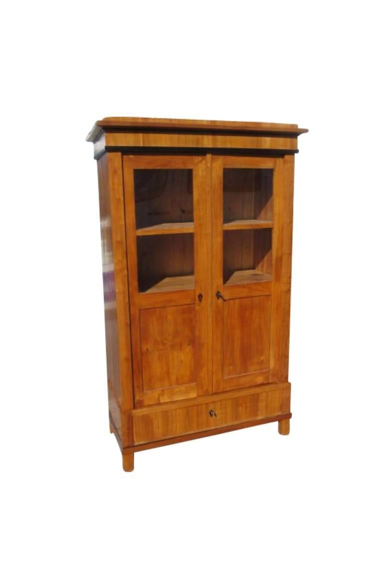 A bookcase from the Biedermeier era made of cherry wood. The, in 1830 manufactured, piece shines in a light brown tone and has a unique grain. The precious wood is treated with shellac to get the best color and durability out of it. Two floors hide