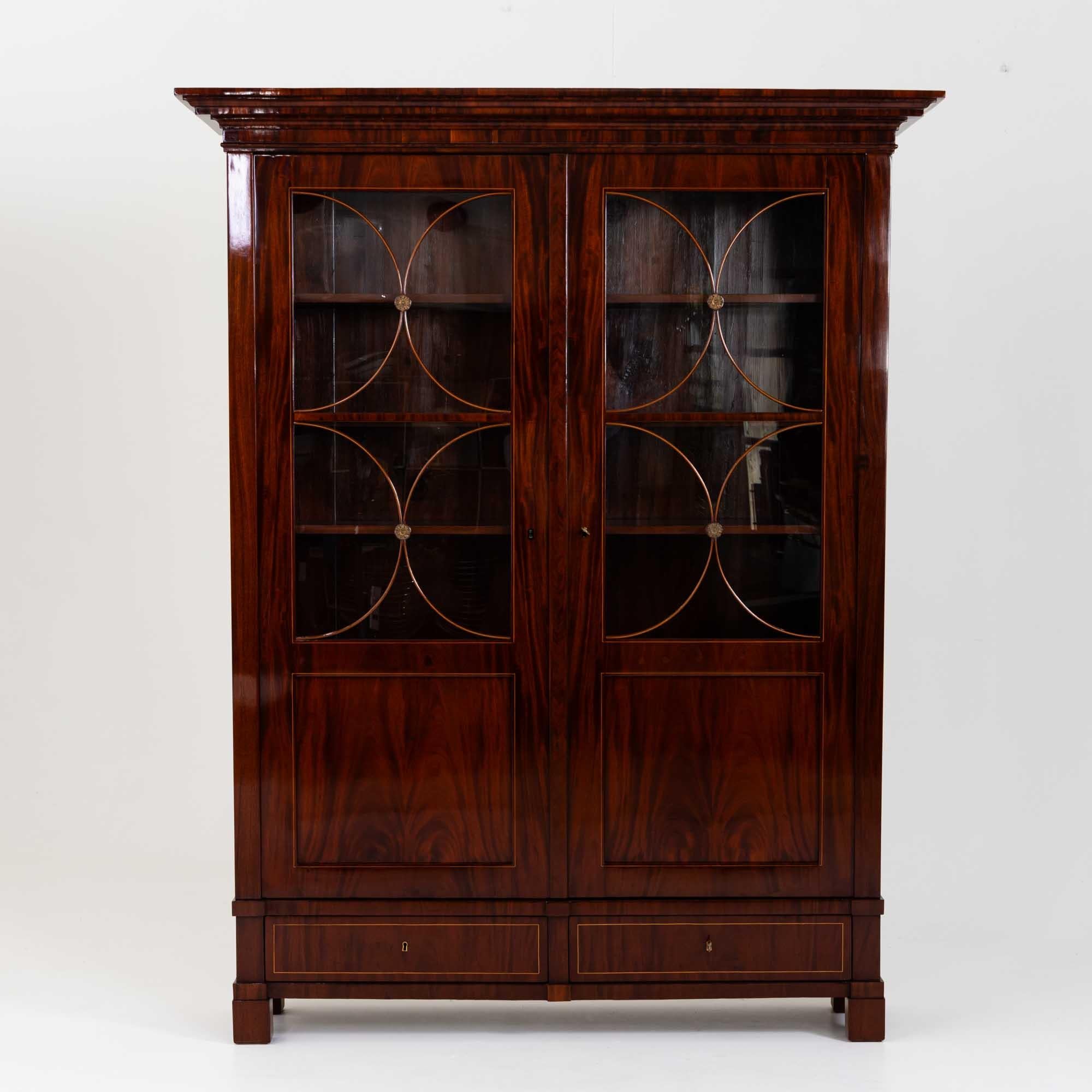 Biedermeier bookcase with a straight, multi-profiled cornice and doors with two-thirds glazing including c-shaped bar, each decorated in the centre with a bronze rosette. The cabinet also has two drawers in the plinth zone and stands on square feet.