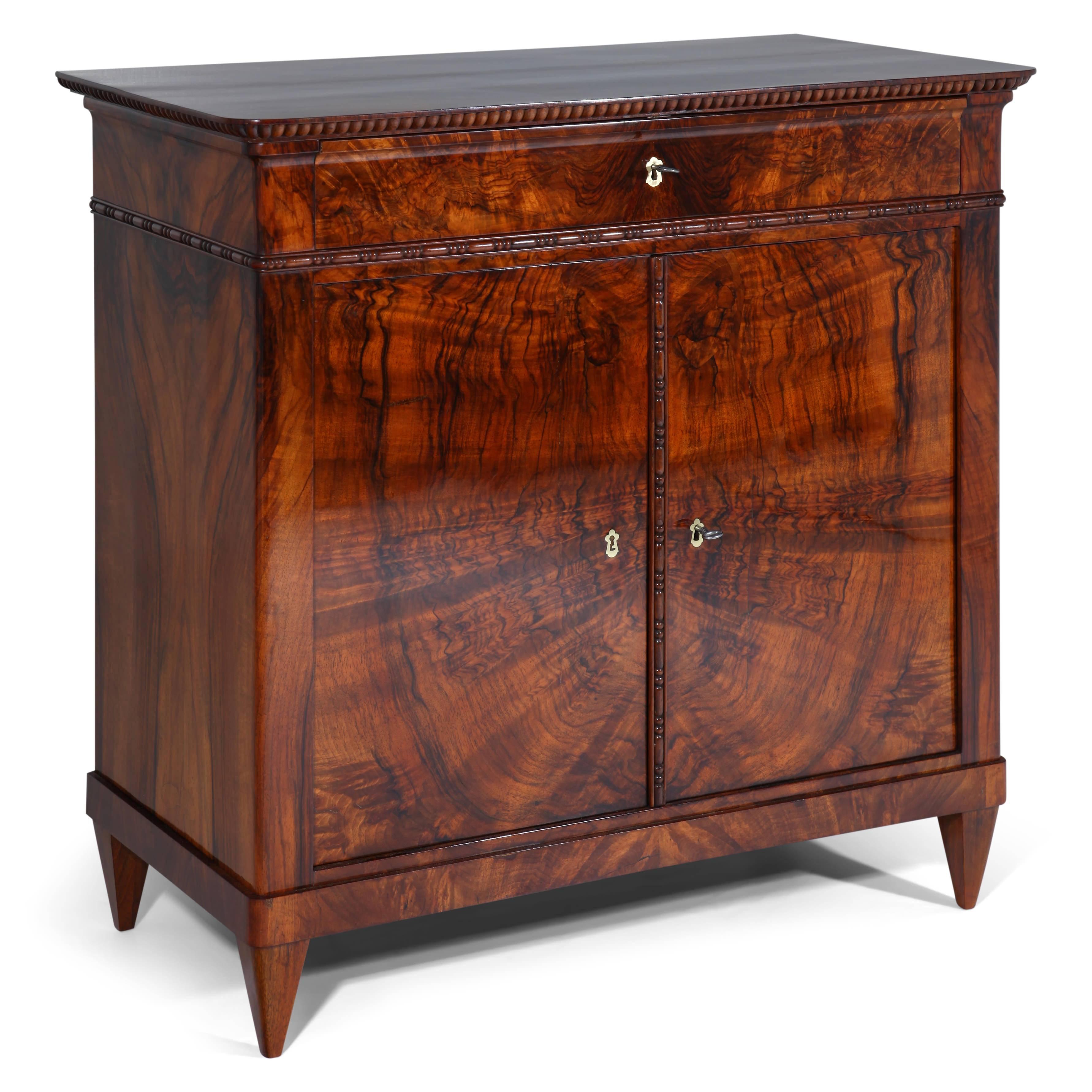 Biedermeier cabinet on tapered feet with two doors and one drawer. The cabinet shows a very beautiful walnut veneer pattern and bead-and-reel moldings.