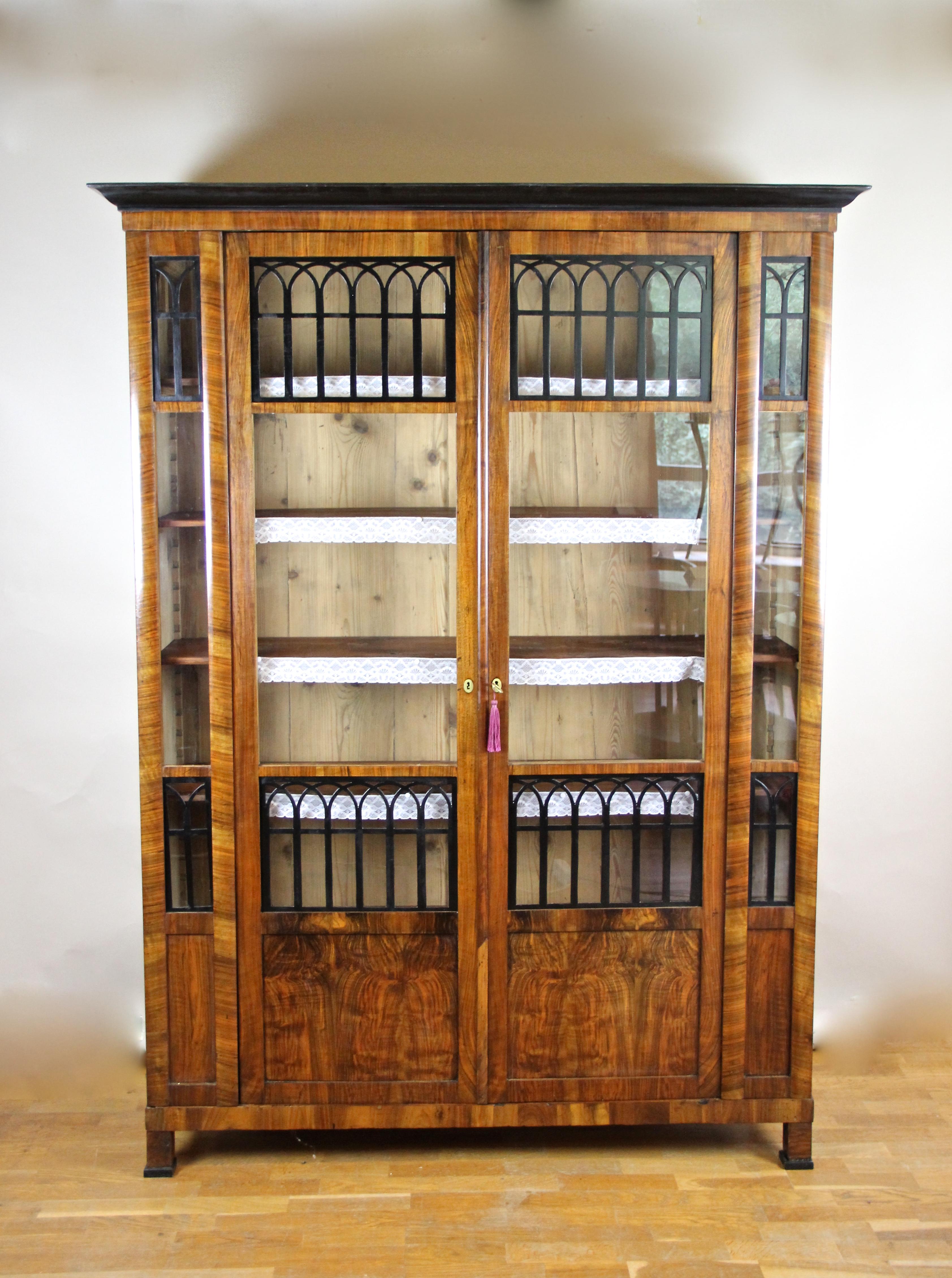 Outstanding Biedermeier cabinet/ bookcase from the renowed Biedermeier era  in Austria around  1830. Veneered in beautiful burr walnut and fine nut wood this slender antique cabinet features two doors with large glass panels which are additionally