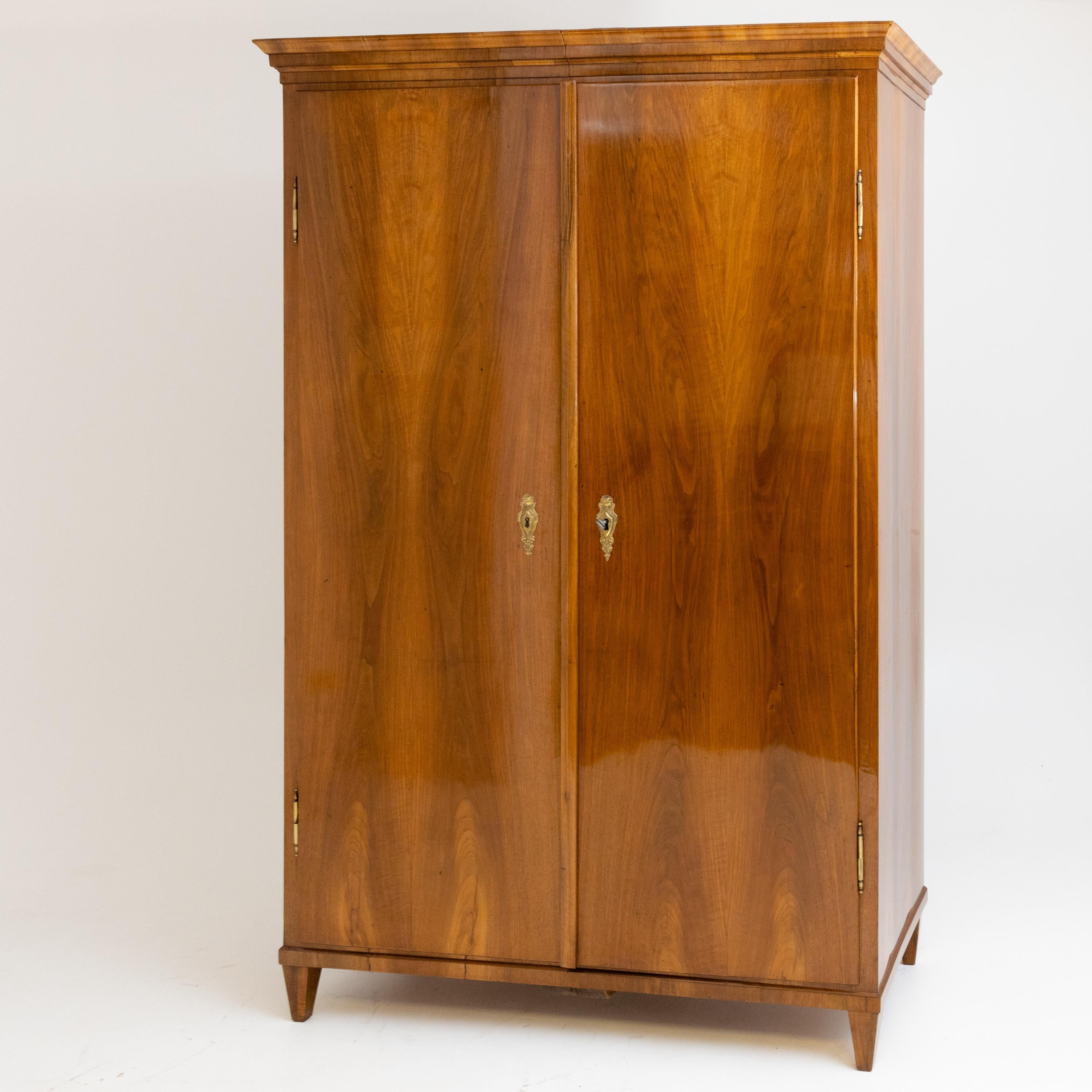 Two-door Biedermeier cabinet in walnut veneered, standing on low tapered legs. The smooth, straight-lined body ends with a profiled cornice. The cabinet has been expertly prepared and hand-polished.