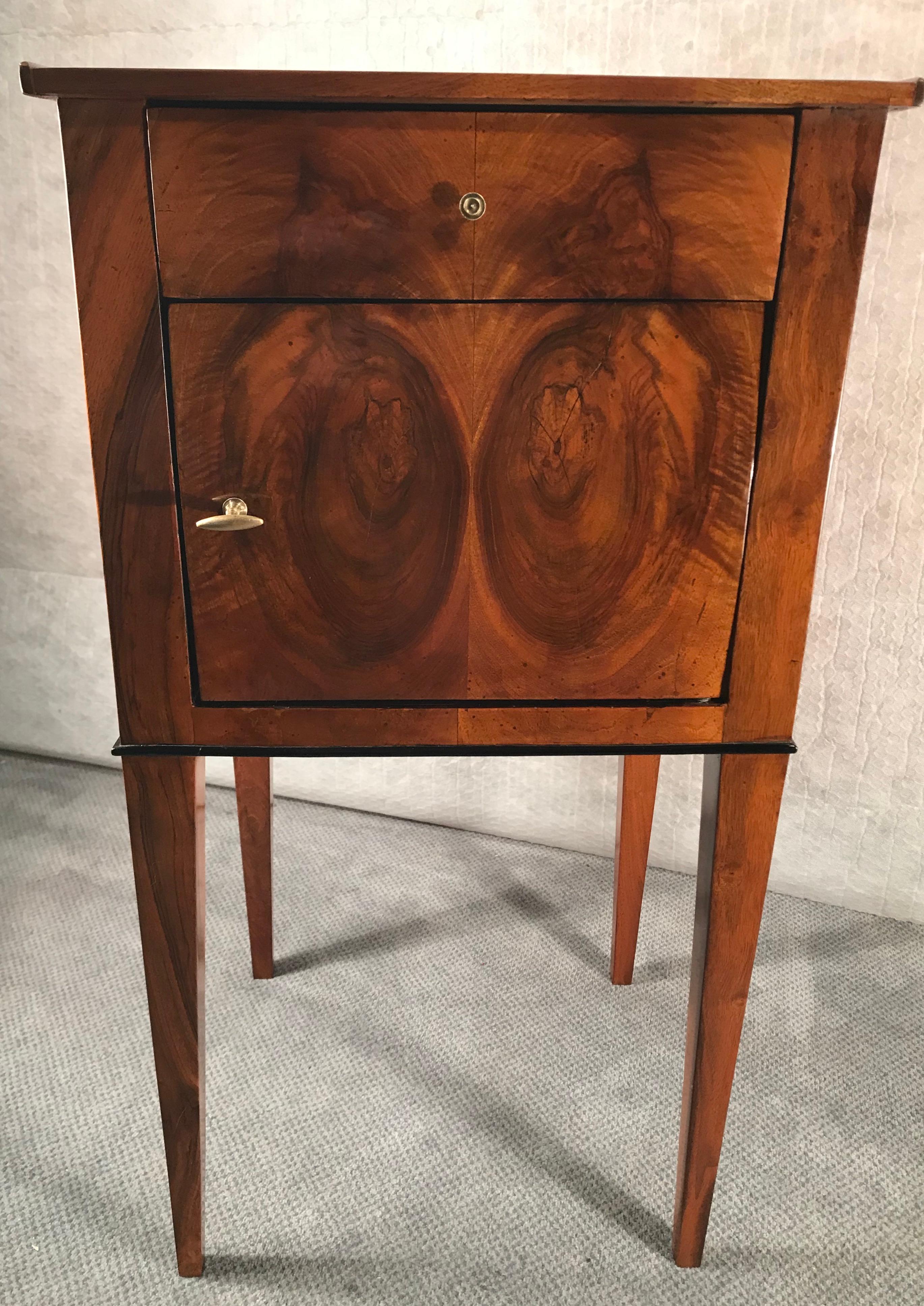 Biedermeier cabinet, South German 1810. Small cabinet or nightstand of the Biedermeier period. The cabinet has a beautiful walnut veneer. It stands on high legs and has one door and one drawer. 
It does not have to be placed against a wall because