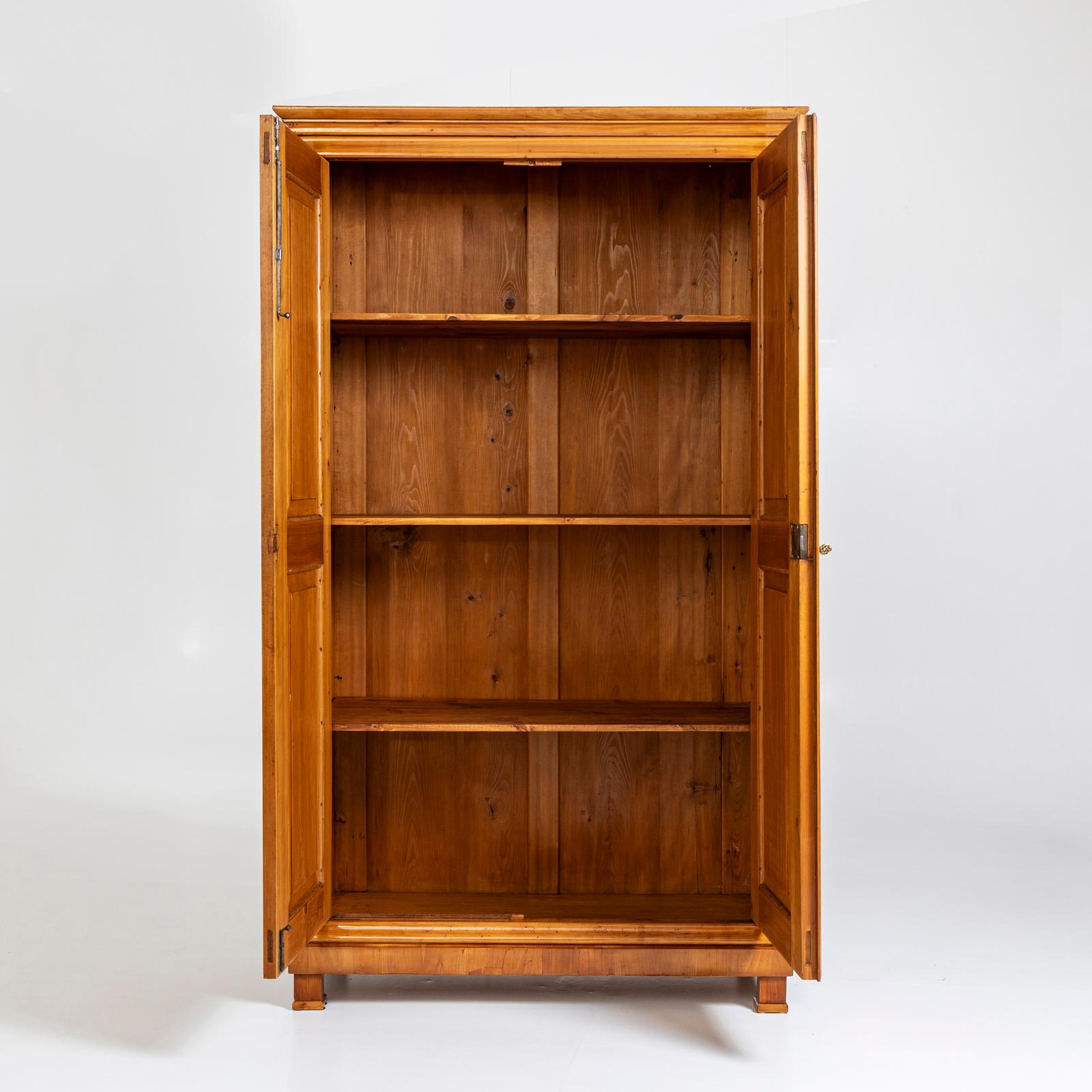 Mobile Biedermeier a due ante impiallacciato in ciliegio e lucidato a mano. I pannelli sono decorativamente incastonati in radica. La divisione interna è composta da tre ripiani. Il gabinetto proviene dall'aristocrazia bavarese. 