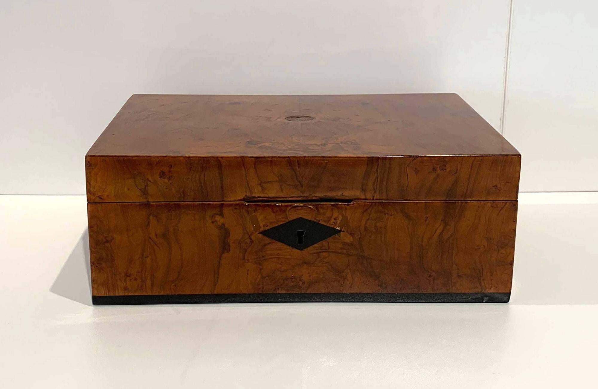 Walnut veneer with ebony ribbon inlay at the lower edge. An imprint in the top center of the lid.
Refinished condition. Polished with shellac by hand for a beautiful high-gloss surface.
Dimensions: H 10.5 x W 28 x D 19 cm