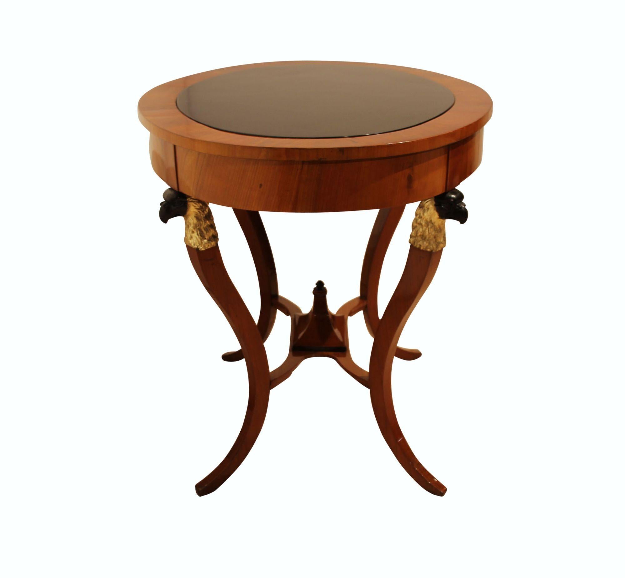 Oval, early Biedermeier / Empire Saloon or Center Table from Vienna, Austria around 1820.
Cherry veneered and solid wood. Intermediate tableau with upward tapering partly ebonized and painted decor.
Four carved eagle heads on the sides, re-gilded