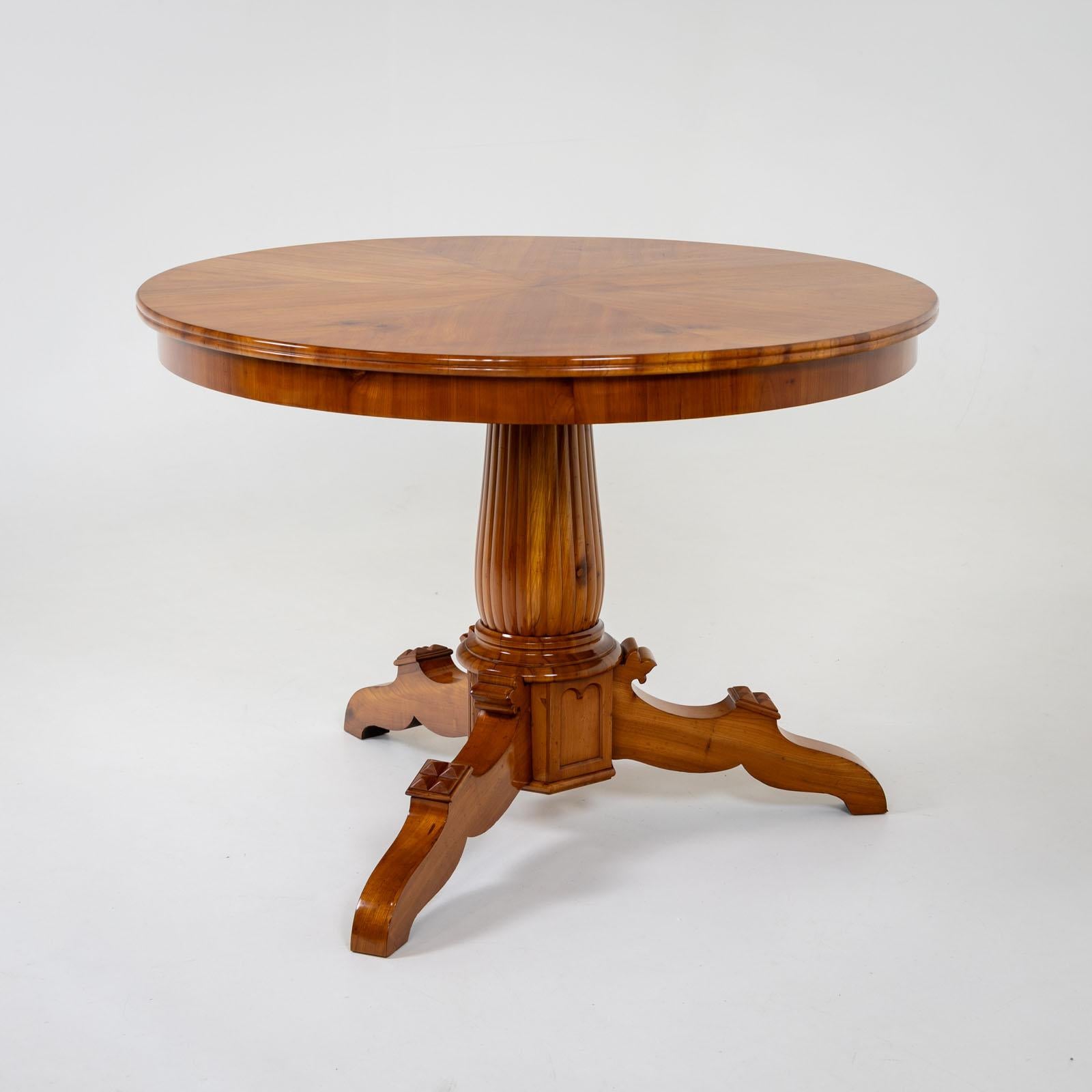 Cherry center table on three curved legs with carved stud decoration and a conical central column with grooved decoration. The round table top is veneered in segments and profiled at the edge. The table has been restored and polished by hand.