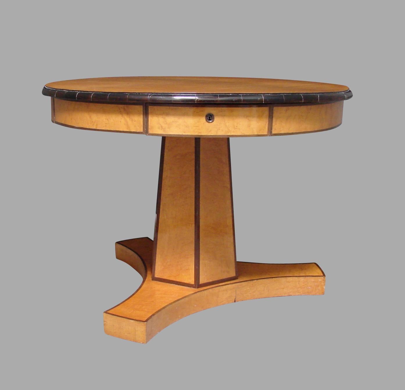 A good quality Austrian Biedermeier satin birch or maple center table, the top with an ebonized edge above 4 functional drawers resting on a hexagonal column ending in a tripod base resting on later casters. This is a stylish and elegant piece of