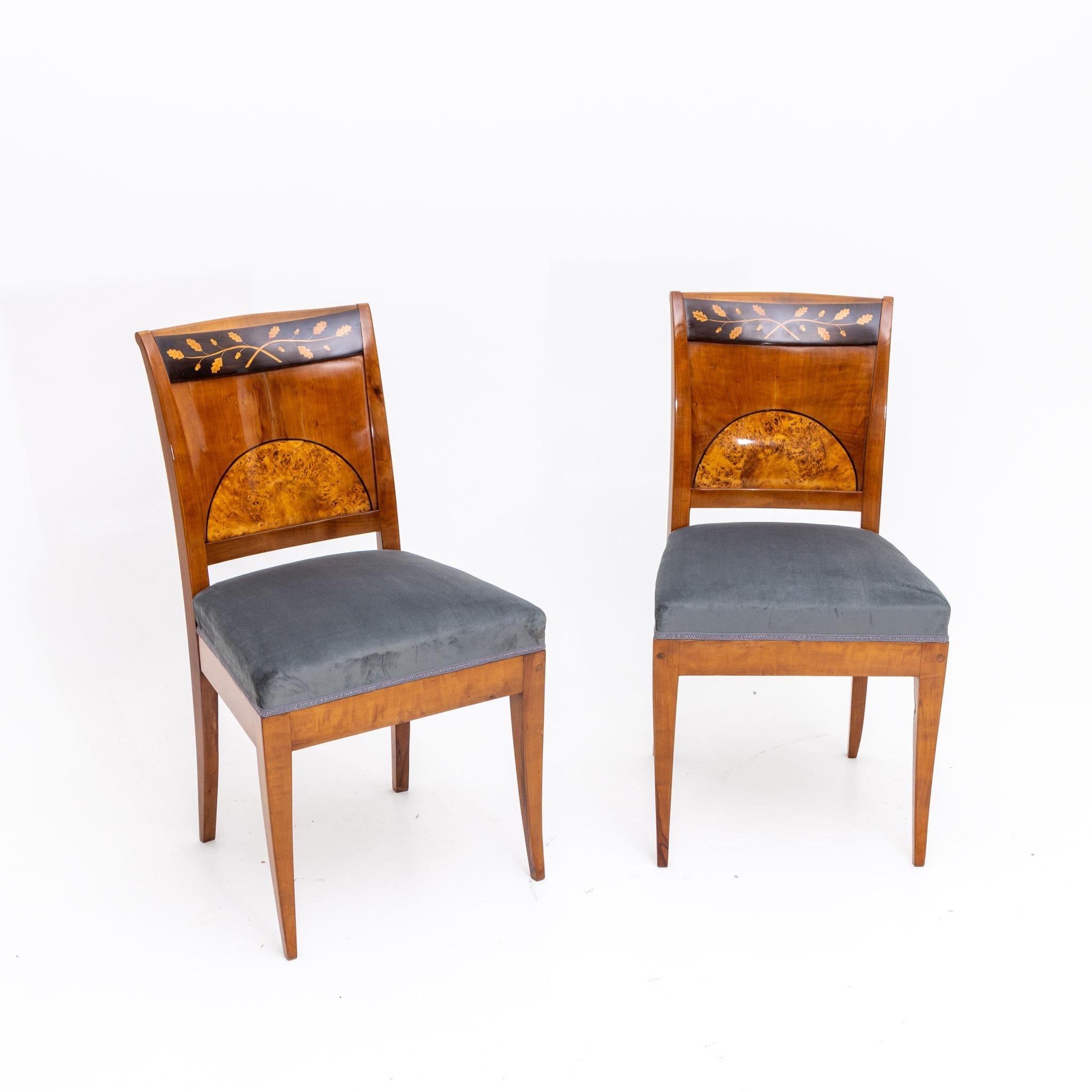 Pair of Biedermeier chairs on flared saber legs and trapezoidal backs with inlay work in the form of a segmental birch burl inlay and oak leaf decoration. The chairs have been reupholstered and hand polished.