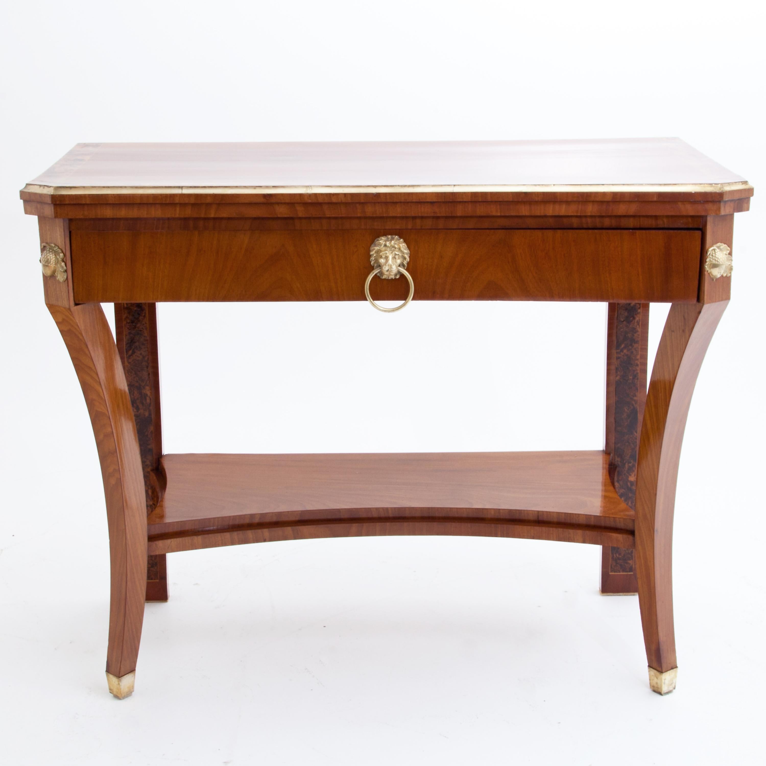 Cherrywood console table on curved square legs with brass sabots, with a drawer under the profiled top with brass band. The rear supports and the edge of the tabletop are inlaid in burl wood. At the corners there are brass fittings in the form of