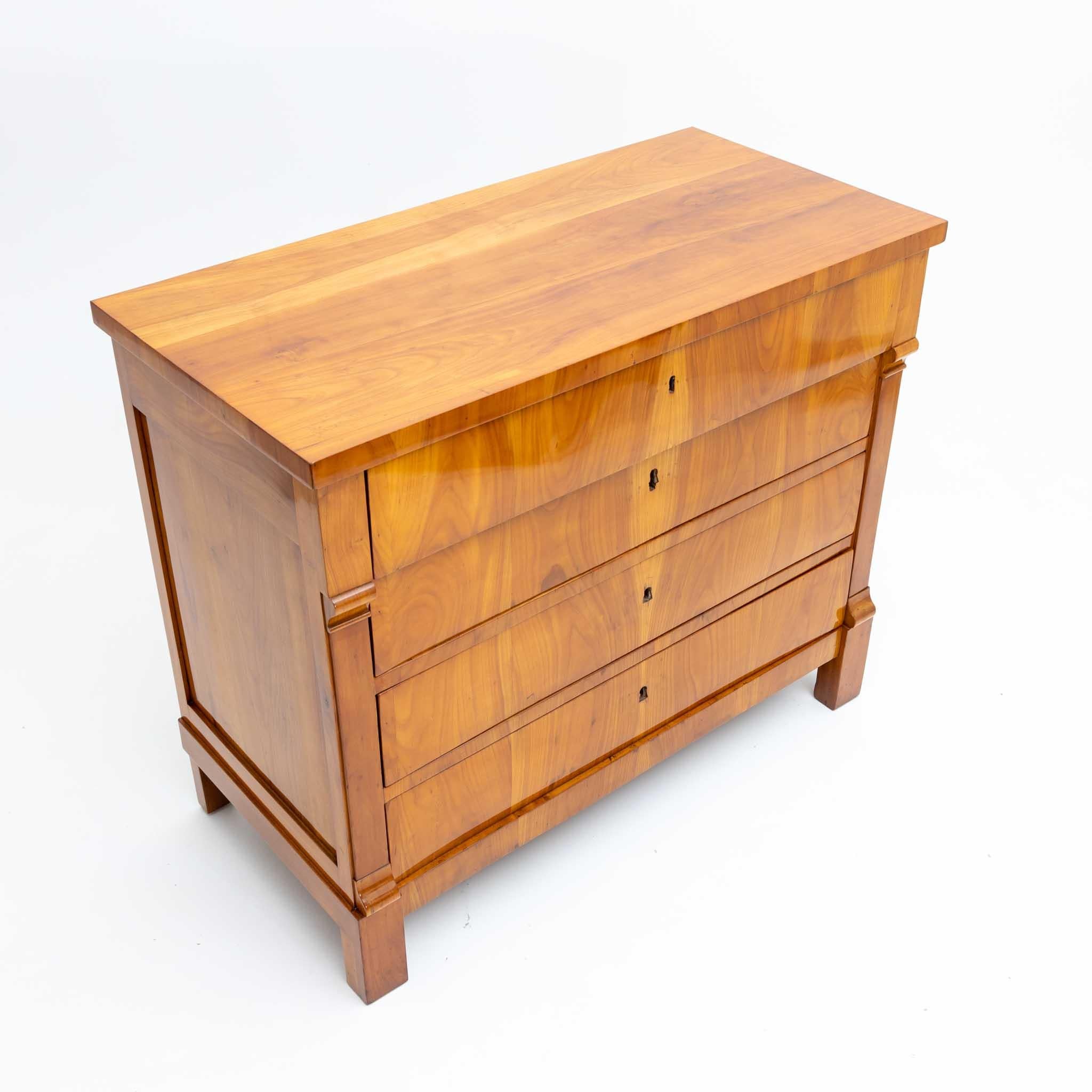 Biedermeier chest with four drawers and indicated pilasters on the corners. The top drawer protrudes slightly and the sides of the corpus are coffered. The chest stands on straight square legs and is veneered in cherry. It has been professionally