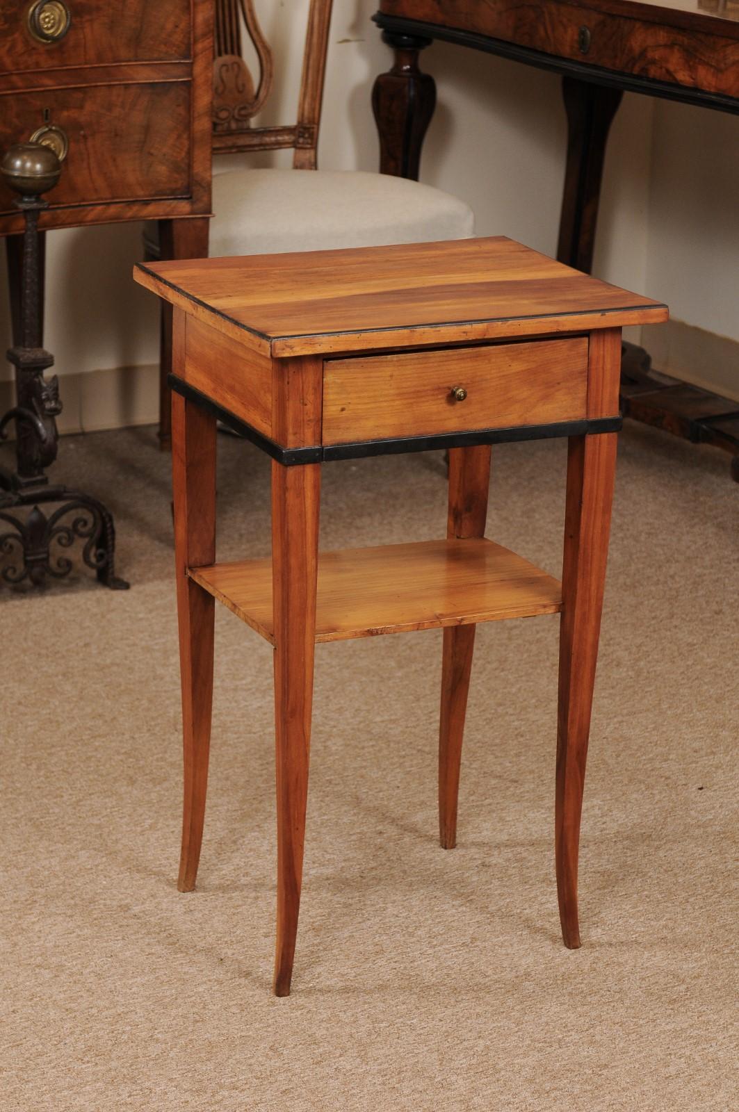 A Biedermeier side table in cherrywood with drawer, ebonized detail and lower shelf ending in tapered splayed legs.