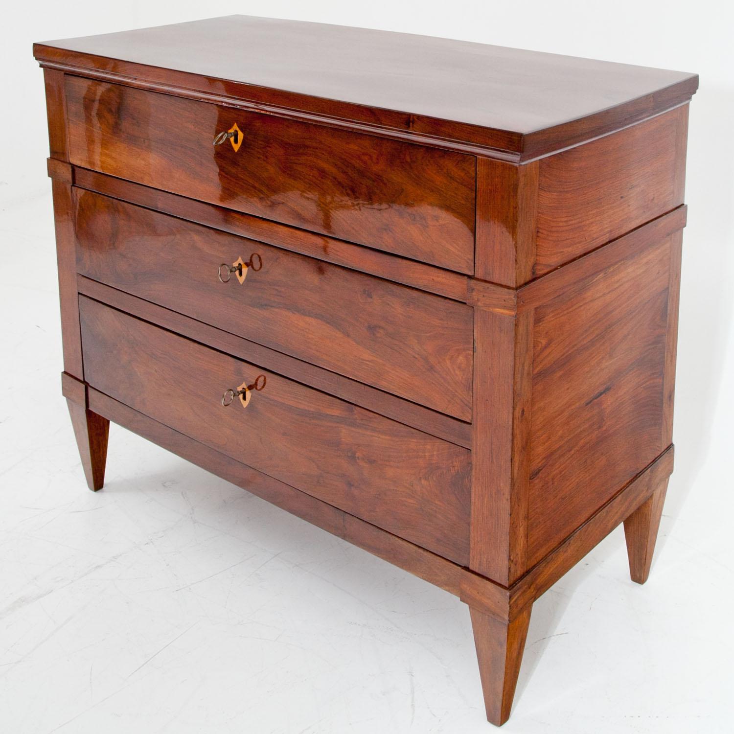 Chest of drawers, standing on tapered legs, with three drawers and escutcheons in maple. The top drawer and the feet are slightly accentuated by rectangles. Walnut veneered. Very beautiful professionally refurbished condition.
