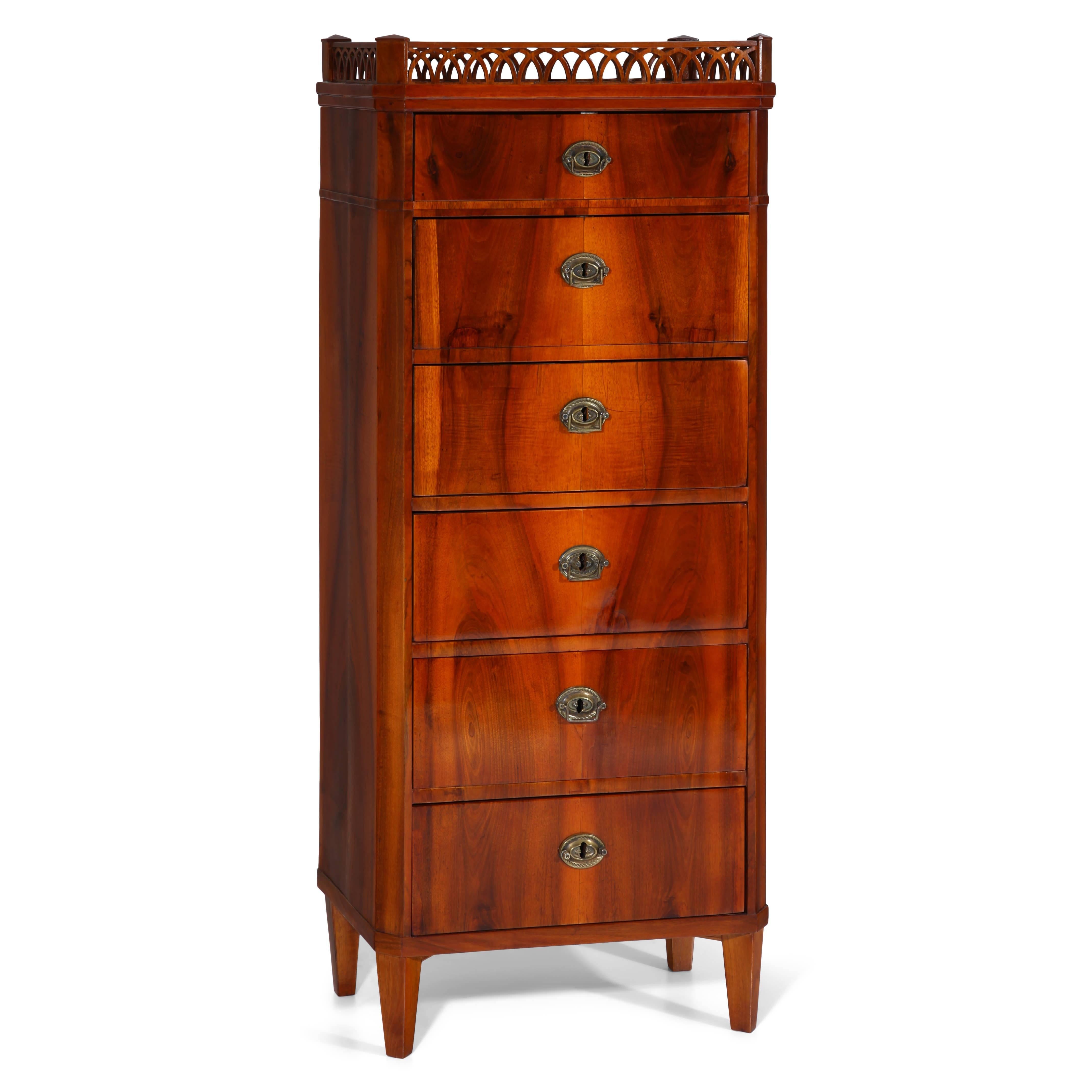 Biedermeier chest of drawers with on short tapered feet. The chest has six drawers and shows a beautiful veneer pattern. The top shows a gallery border with pointed arches.