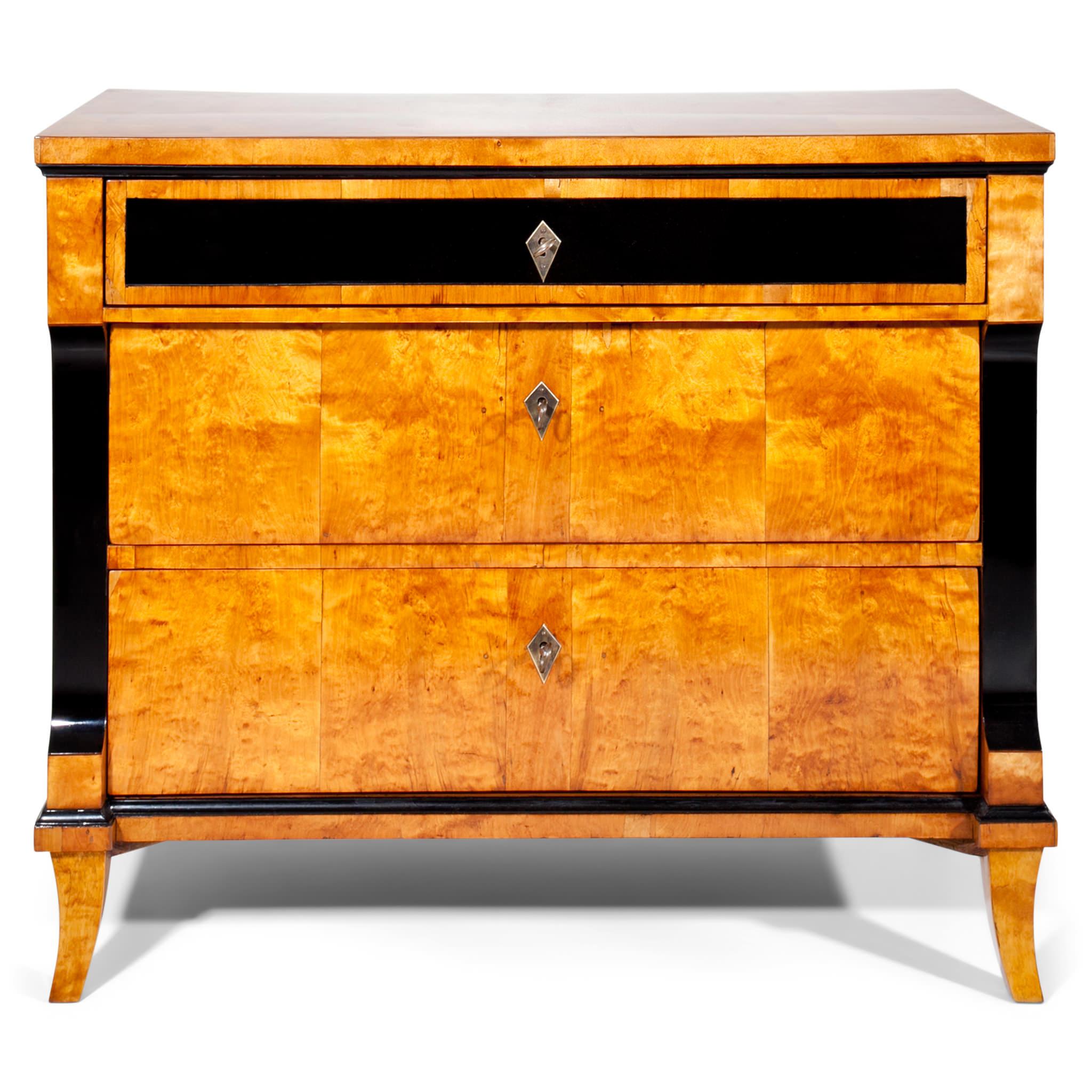 Biedermeier commode with three drawers, standing on short tapered feet. The body is veneered in birch tree and shows ebonized décor such as on the top drawer and the profiles.