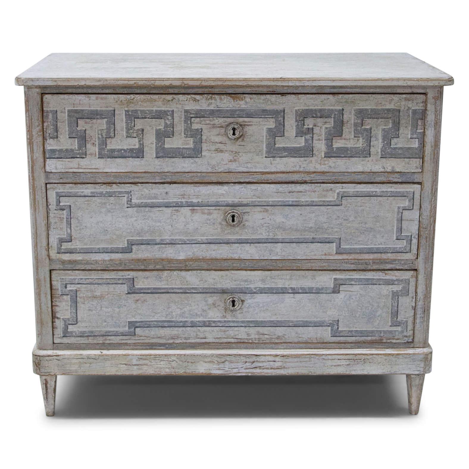 Three-drawer Biedermeier chest of drawers on short tapered feet with a streamlined body and rounded corners. The Gustavian-style paintjob is new and shows Meander décor on top and fillings in grey on white ground. The paintjob has a used-looking