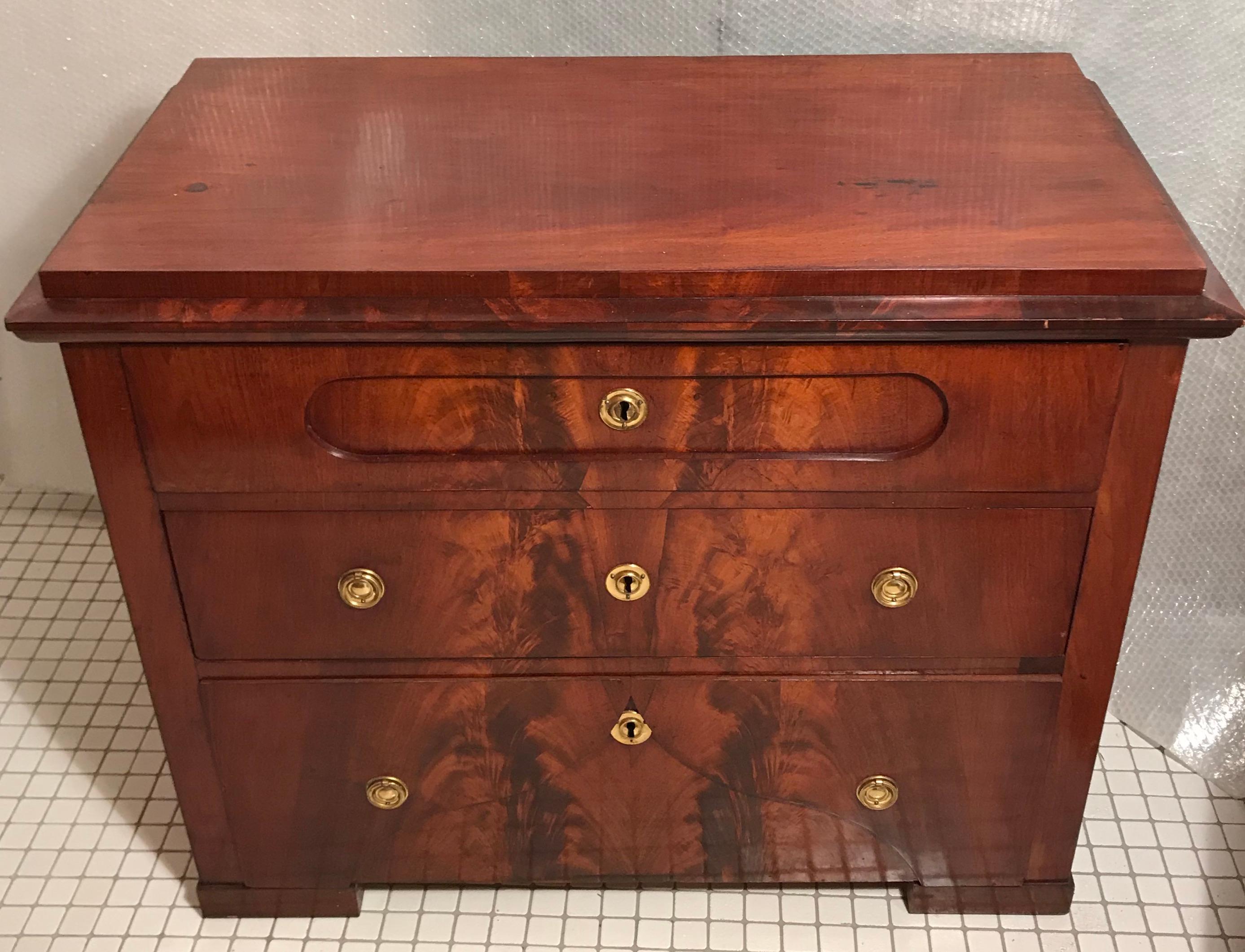 Biedermeier chest of drawers which stands out for its beautiful mirrored mahogany veneer was made in Denmark around 1820. It has three drawers and original brass fittings. It is in very good, refinished and French polished condition. The commode