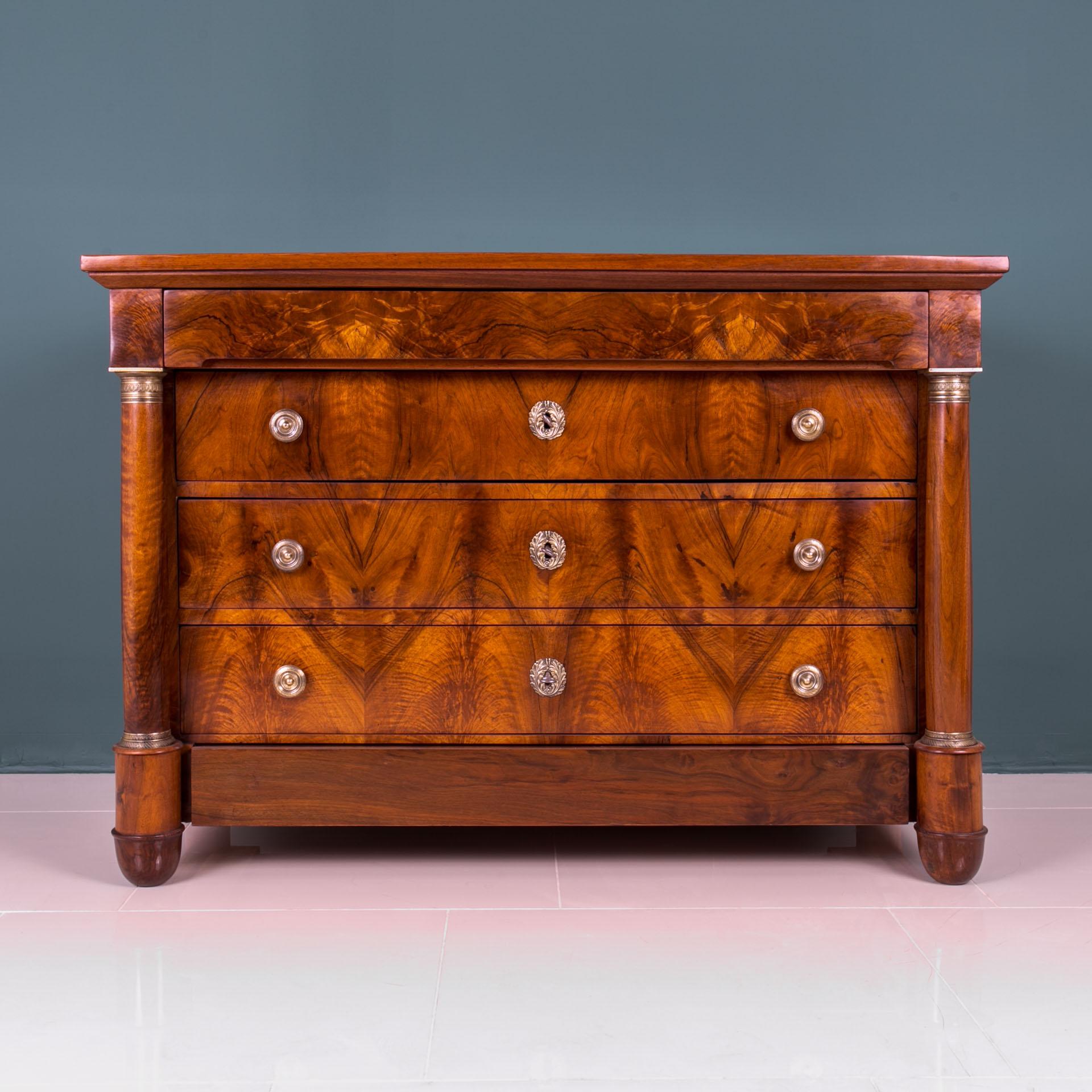 Biedermeier chest of drawers from 19th century, circa 1830s. This piece of furniture comes from France. It was made of softwood and veneered with beautiful walnut veneer. It is equipped with unique columns, decorated with brass decorations. It has