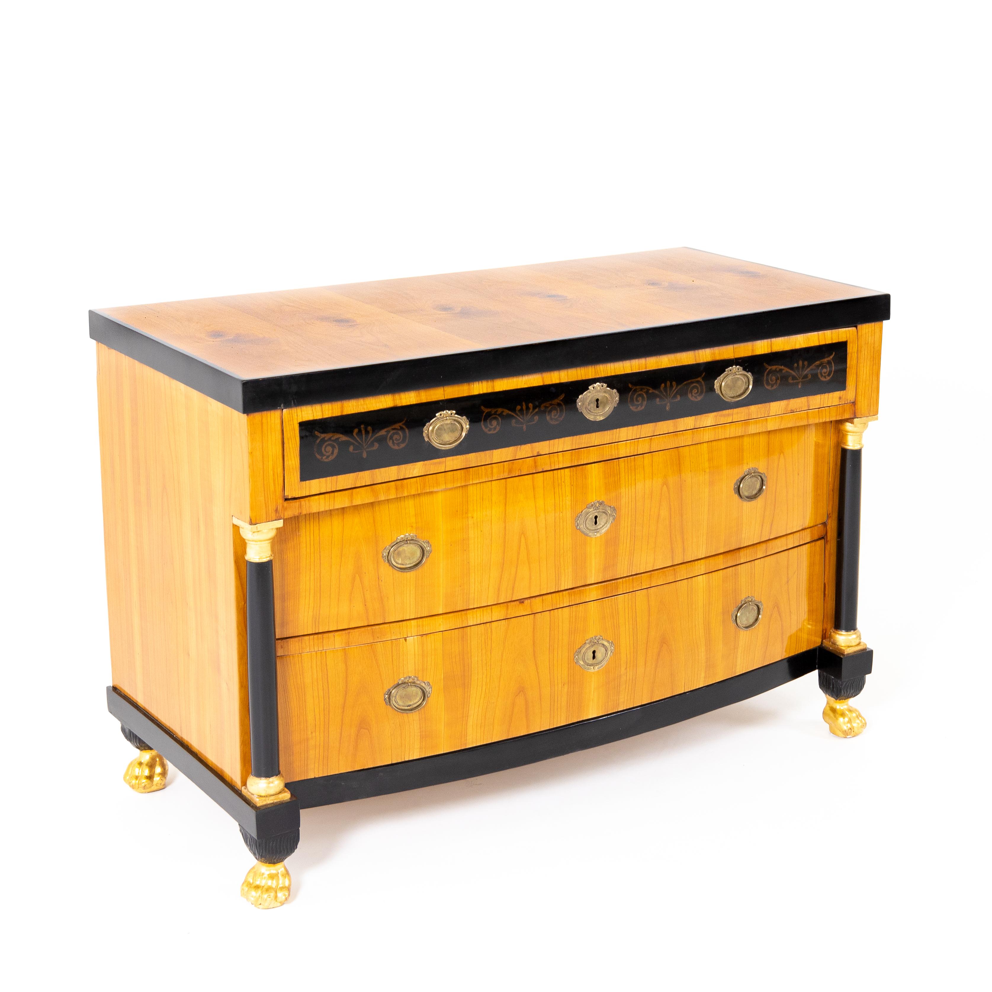 Three-drawered chest of drawers on gold-patinated paw feet, with bow front and ebonized columns with gilded capitals. The top drawer rests on the columns and is painted with vines against an ebonized ground.