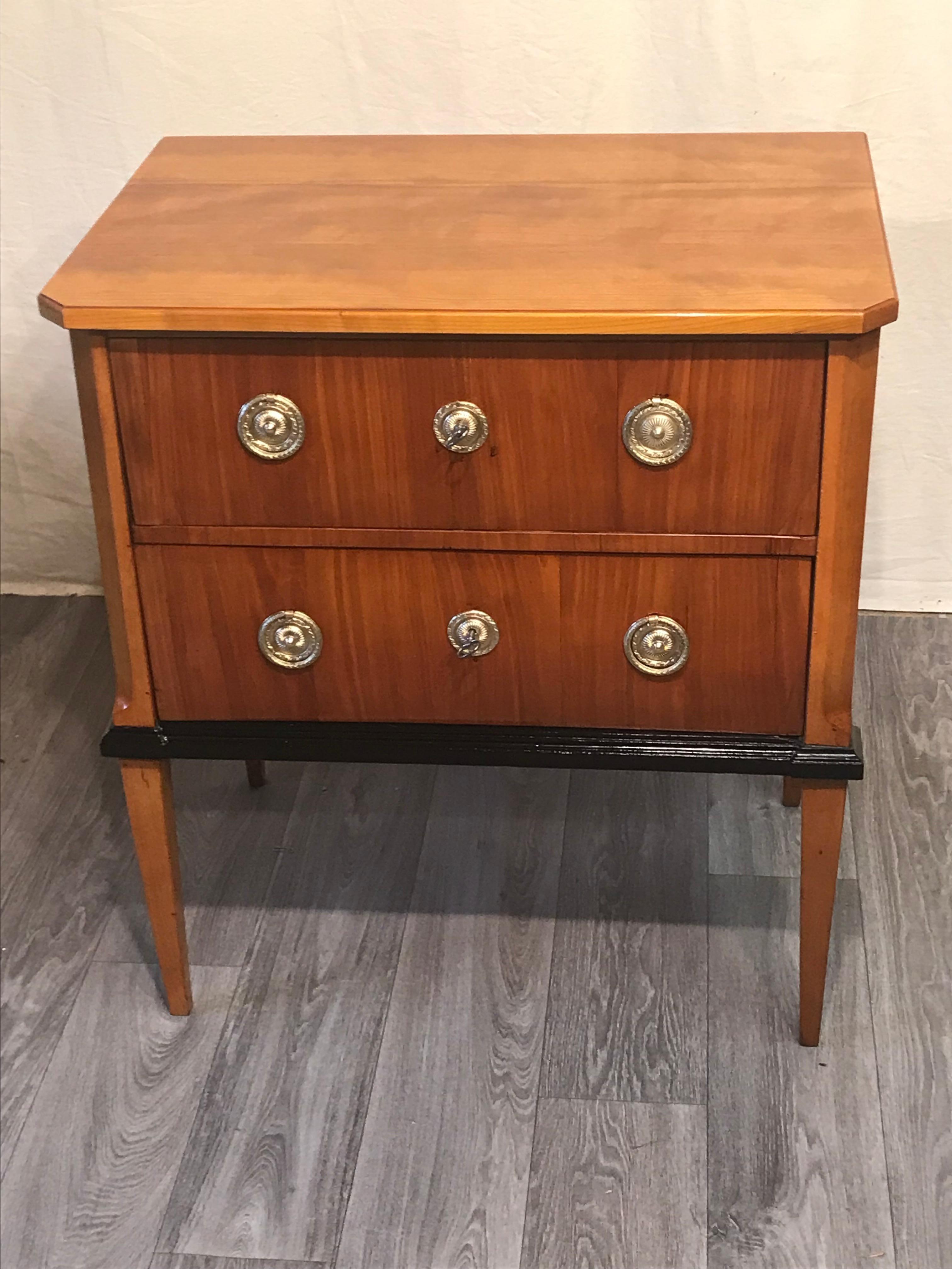 This elegant small Biedermeier chest of drawers comes from Southern Germany and dates back to 1830. The two drawer dresser stands on four pointed legs. It is decorated with cherry veneer and has ebonized details. 
It comes refinished and shellack