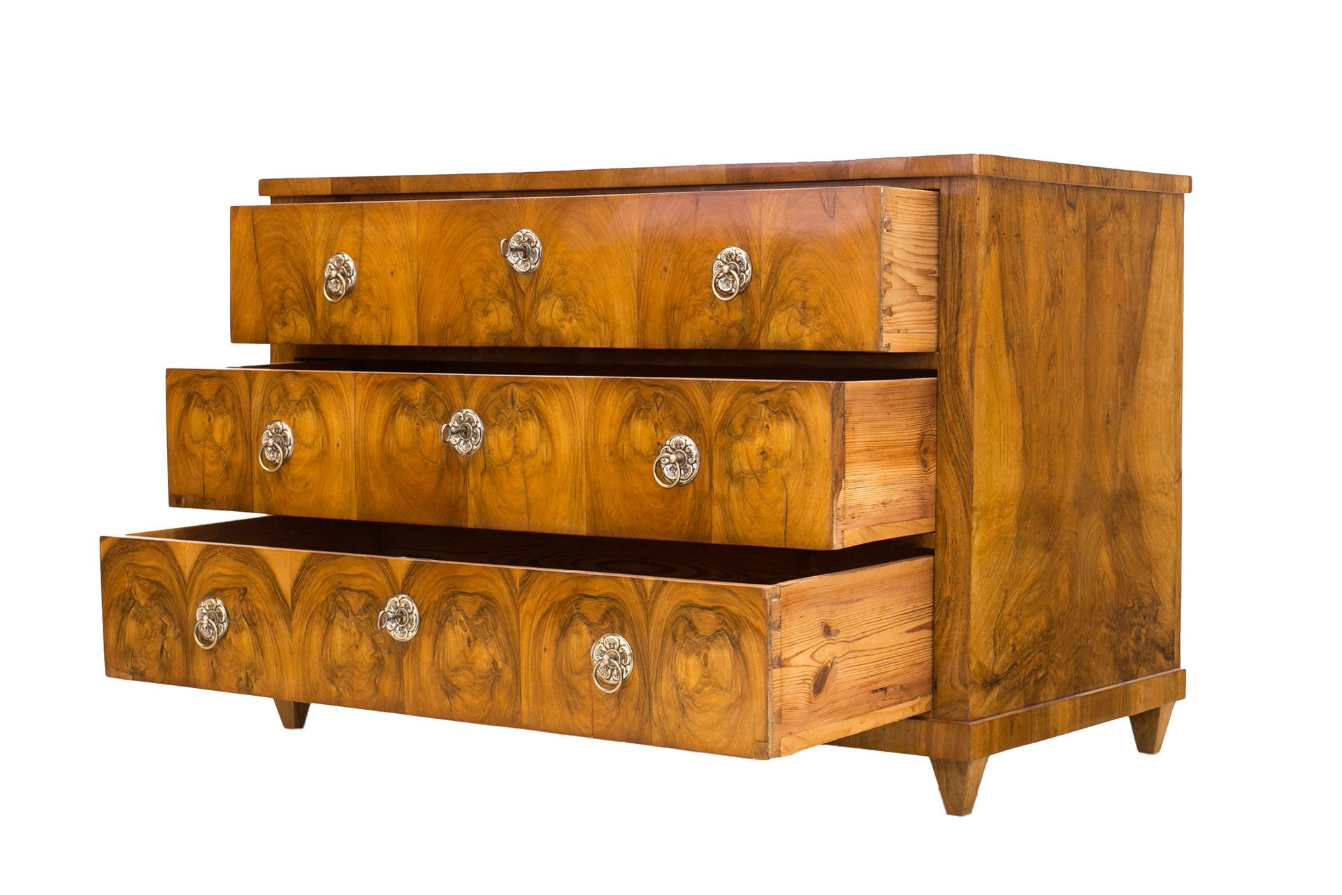 This is an original three-drawer chest of drawers from the Biedermeier period. It was made, circa 1830-1835 in Germany. The piece is made of coniferous wood, veneered with walnut wood. Finished with shellac varnish, hand-applied high-gloss tampon