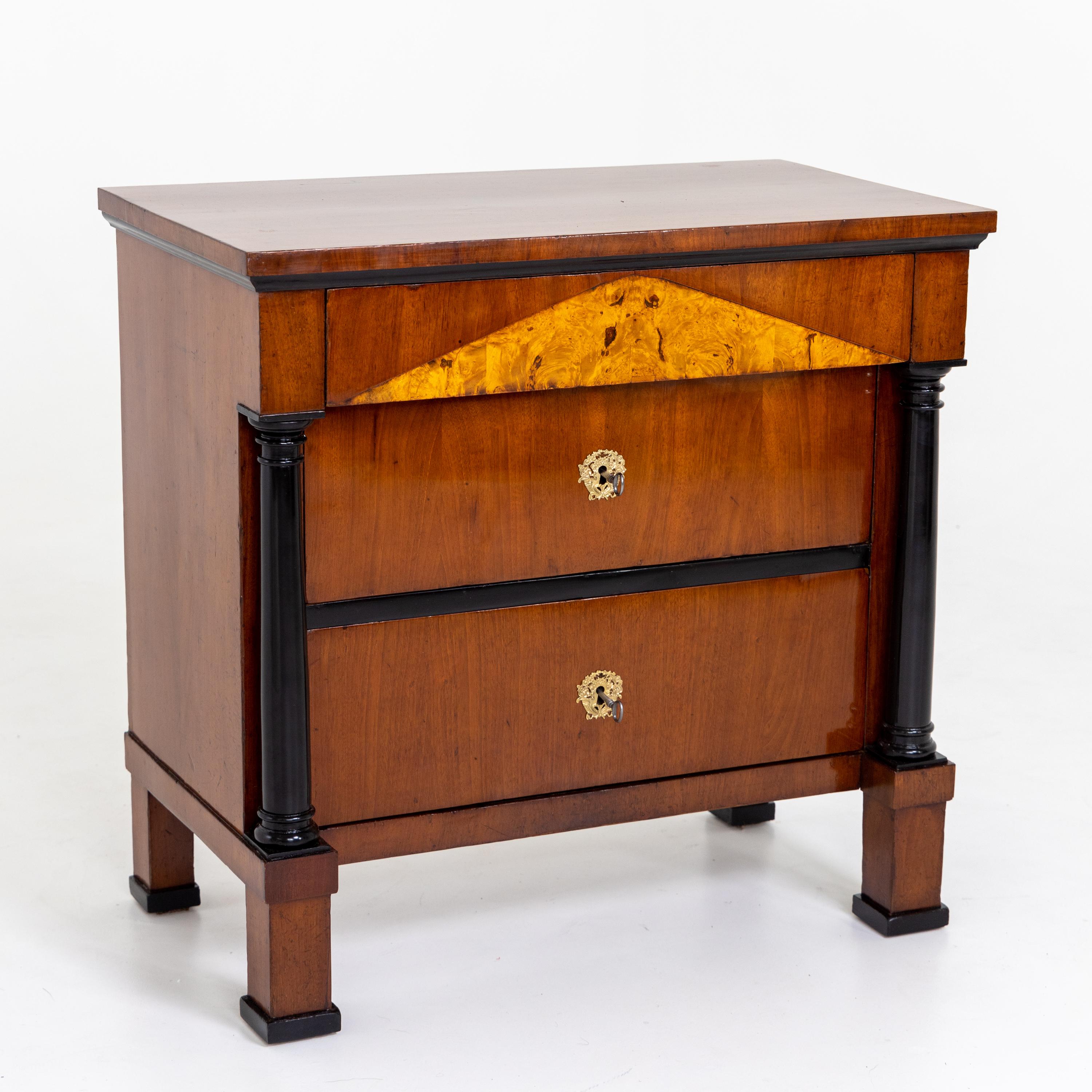 Biedermeier chest of drawers in mahogany with ebonized columns and three drawers standing on socketed square feet. The head drawer with pediment inlay in burl wood.

 