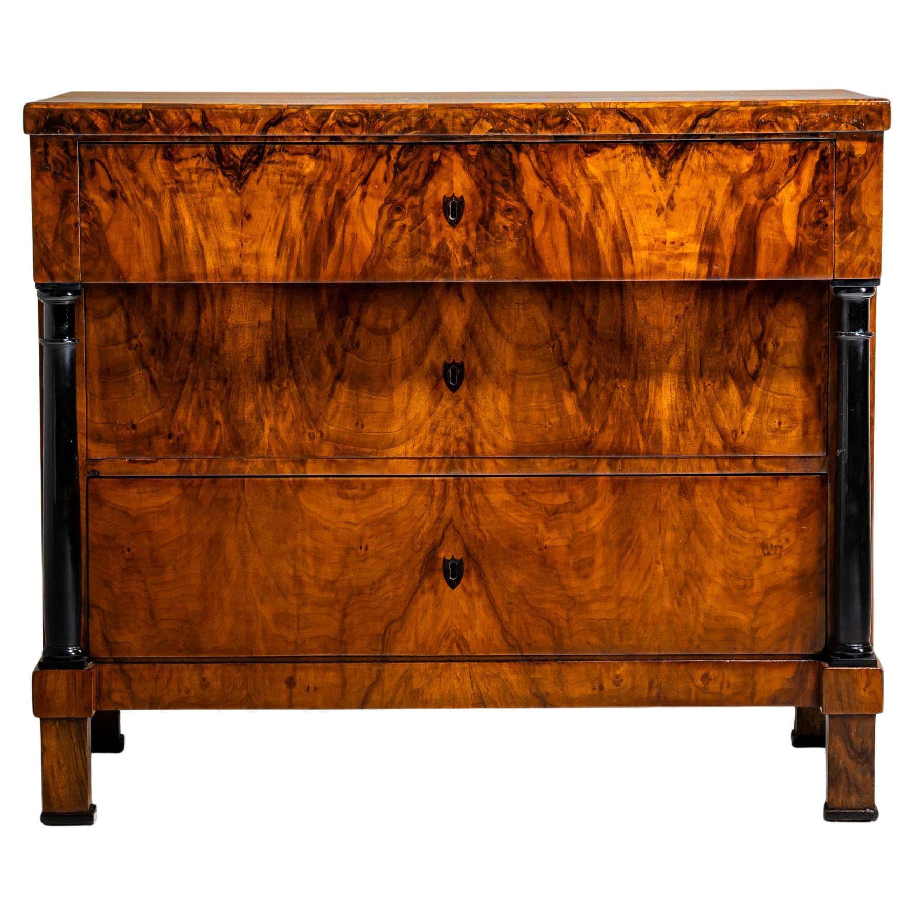 Cassettiera Biedermeier impiallacciata in noce, sollevata su piedi a blocco con colonne piene ebanizzate. Il cassetto superiore sporge leggermente e si appoggia ai capitelli delle colonne. Anche le chiavi a forma di scudo sono ebanizzate. Restaurato