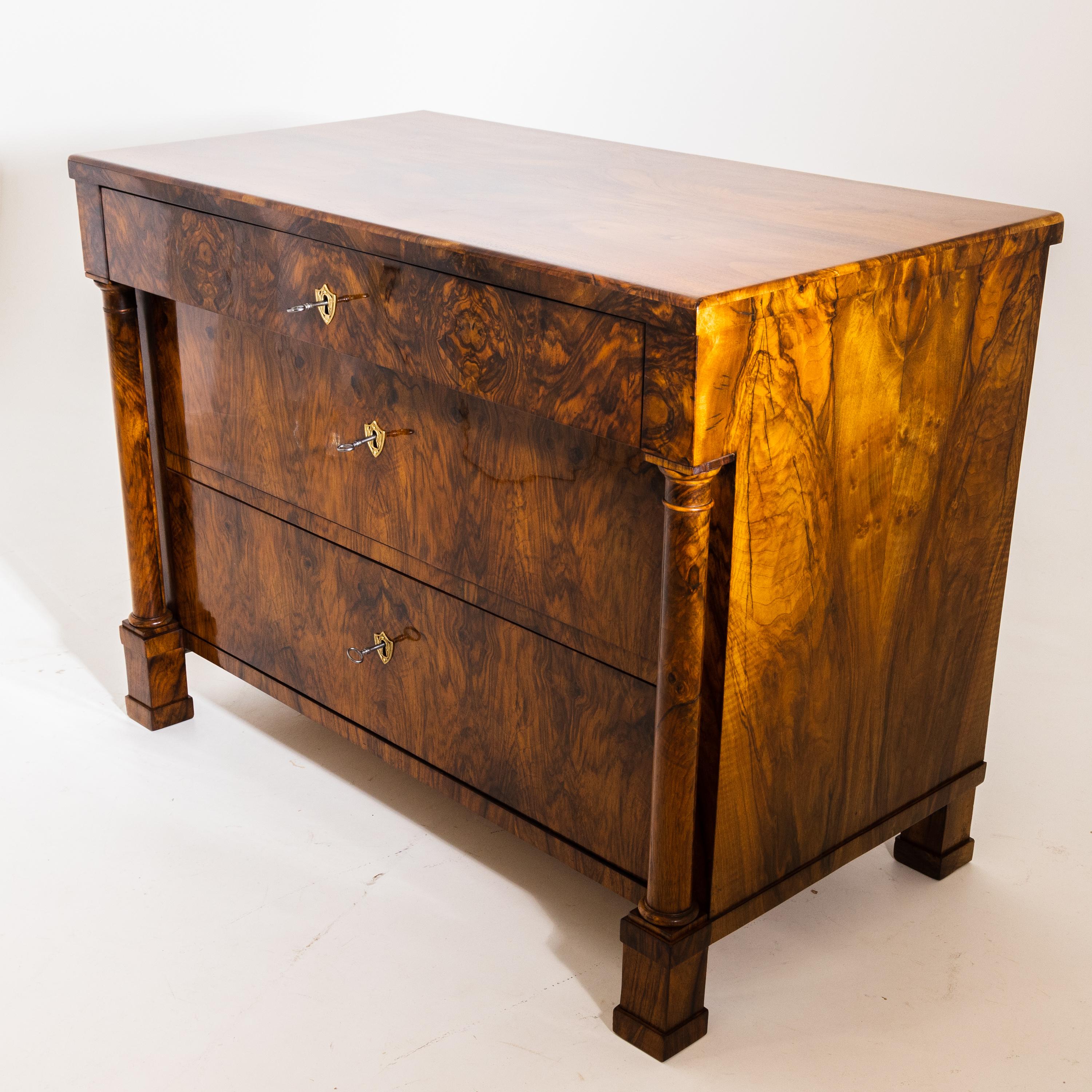 Three-drawer Biedermeier chest of drawers with full-columns standing on socketed square legs. The top drawer protrudes slightly and rests on the columns. Very beautiful walnut burl veneer, hand polished and professionally prepared.