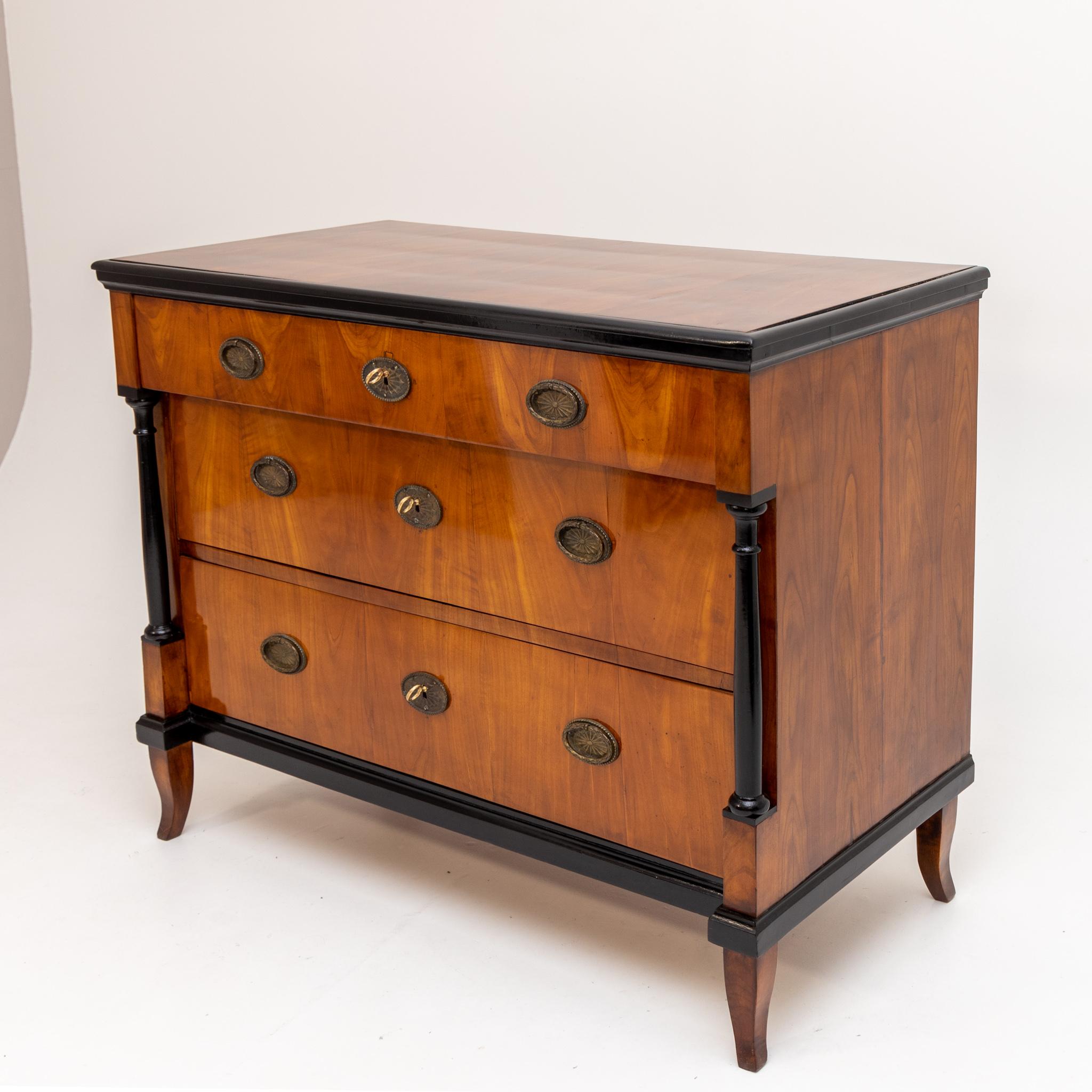 Three-bay Biedermeier chest of drawers on s-legs with ebonised columns and profiles. The corpus is veneered in cherry.