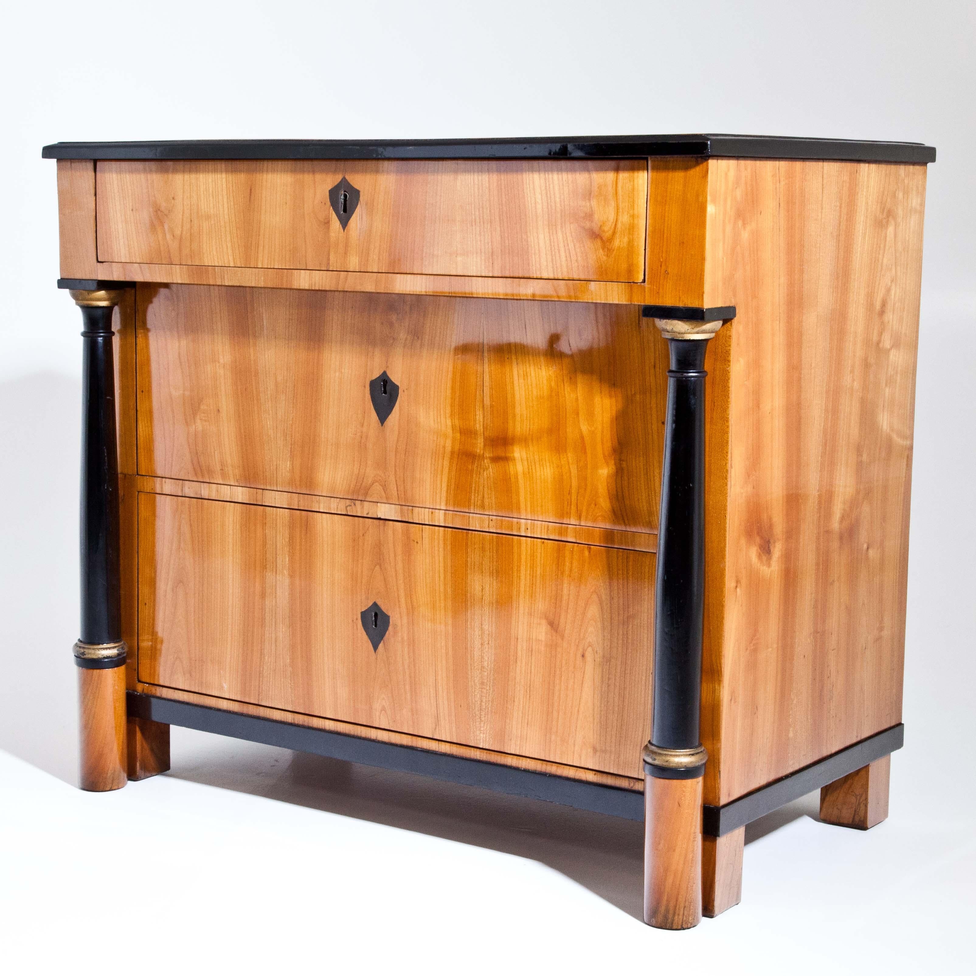 Biedermeier chest of drawers in cherry veneered with ebonised and partly gilt columns, supporting the protruding top drawer. The escutcheons and edges are ebonized. The chest of drawers has been expertly prepared and hand polished.