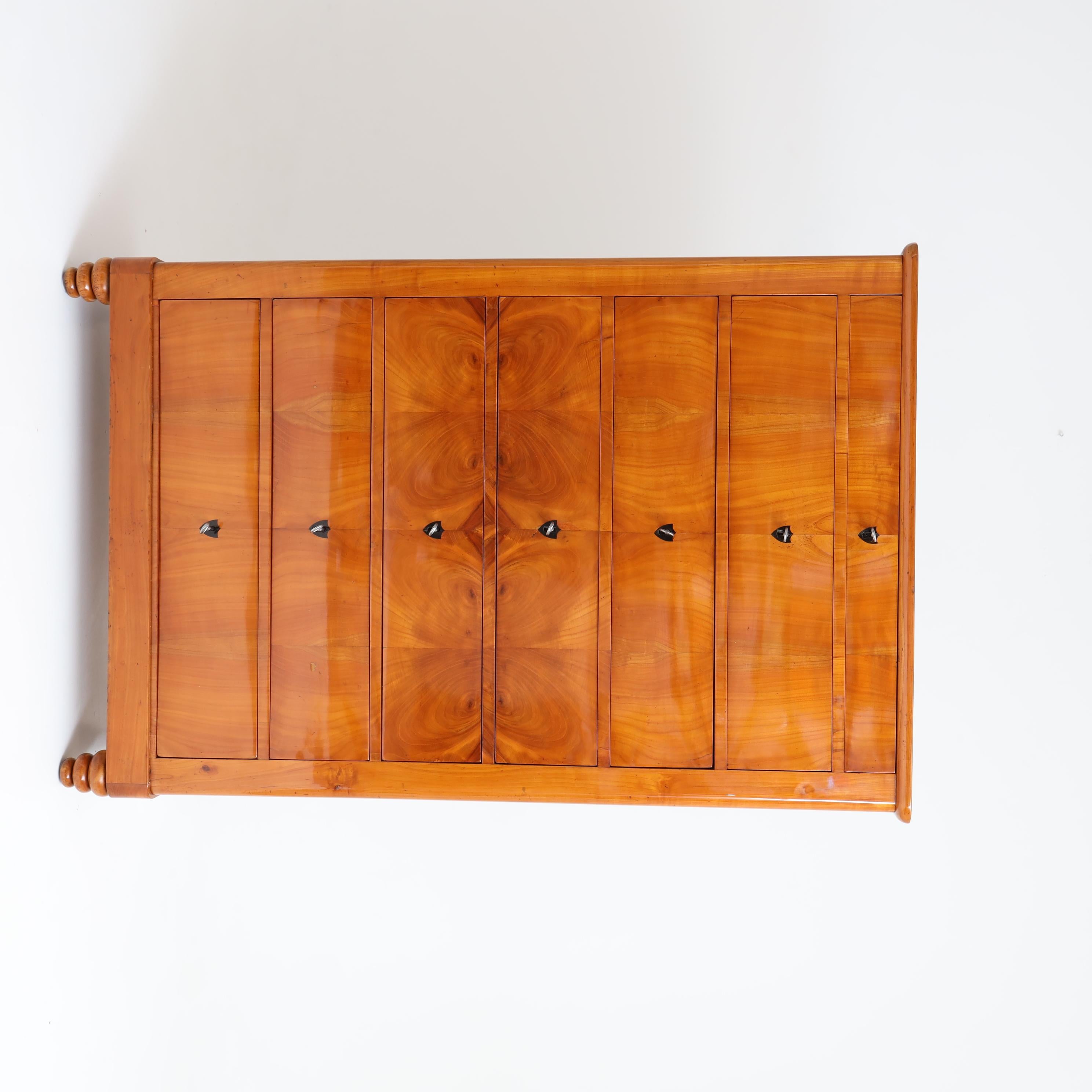 Biedermeier dresser with seven drawers and mirrored veneer pattern in cherry and ebonized eschuchteons. The chest of drawers stands on conical legs and was hand polished.