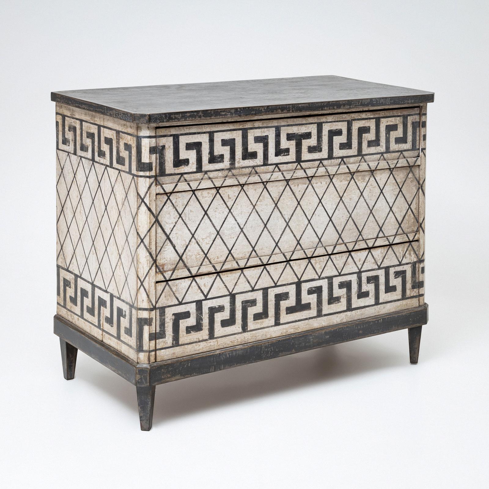A three-drawer Biedermeier chest of drawers made from pine, featuring a newly applied black-and-white color scheme. The decoration includes intricate meander patterns and a diamond grid design. The surface was subsequently antiqued with a patina,