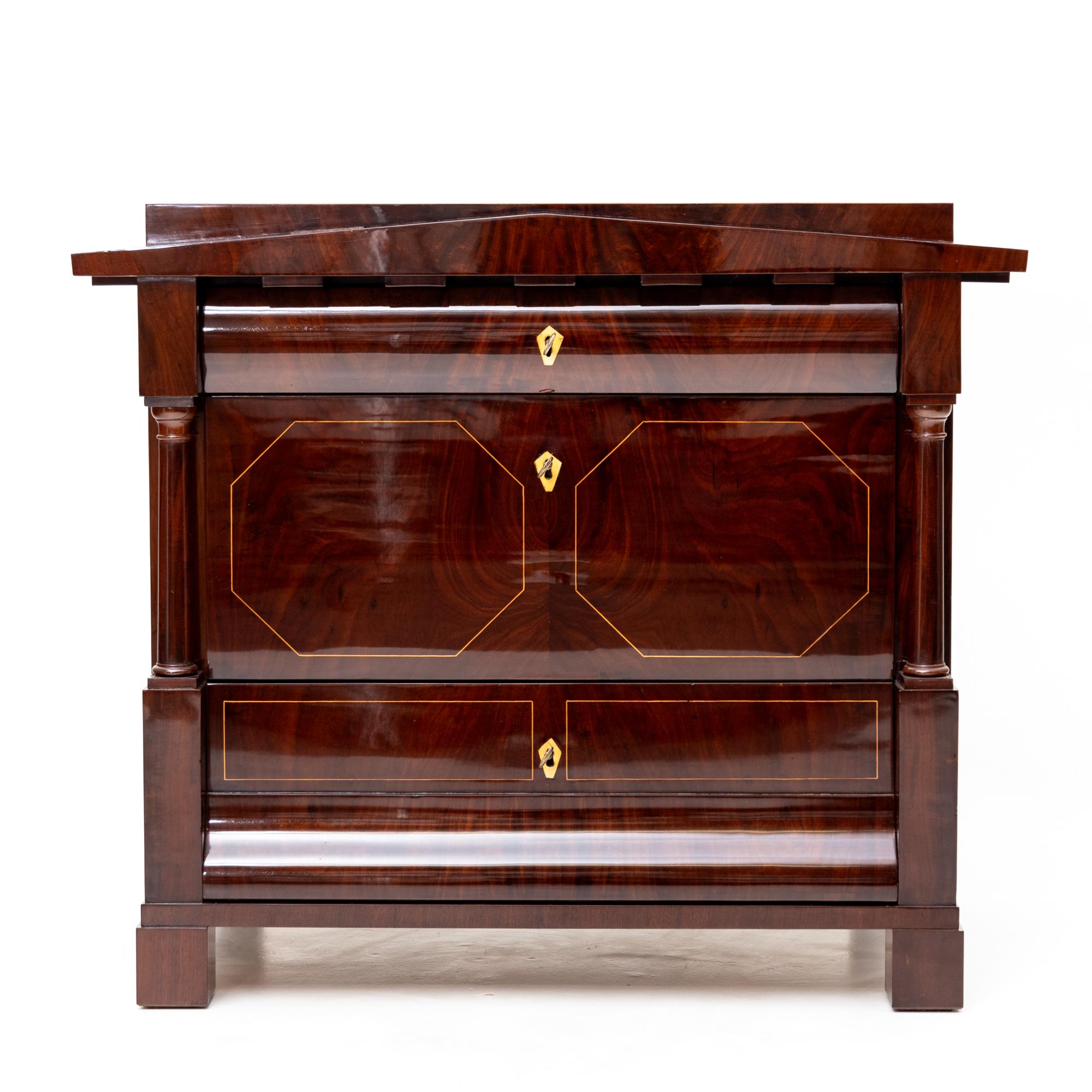 Biedermeier chest of drawers veneered in mahogany with light thread inlays on the front. The dresser features a triangular pediment with dentil frieze and is flanked on the sides by two column inlays. The matching wall mirror is also decorated with