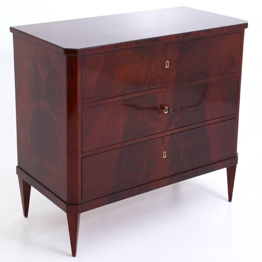 Three-drawered Biedermeier chest of drawers, standing on tapered feet. The keyholes have brass linings and the corners of the body are slanted. The chests shows a very nice mahogany veneer.