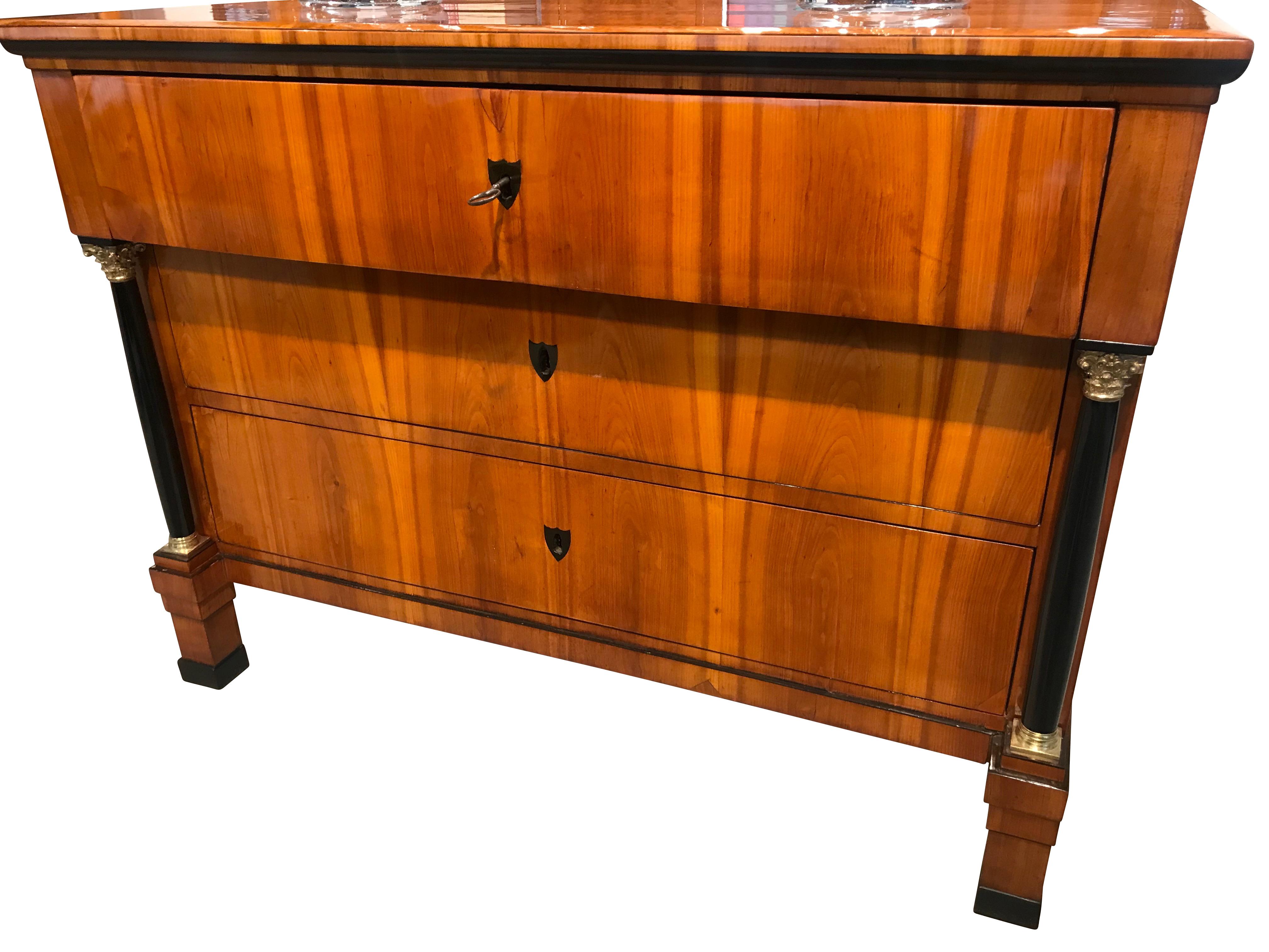 Elegant Biedermeier Commode/Chest of Three Drawers from South Germany around 1825.
The commode has two ebonized full columns with corinthian brass capitals and bases.
Everything including the locks is original. 

The cherry veneer is very