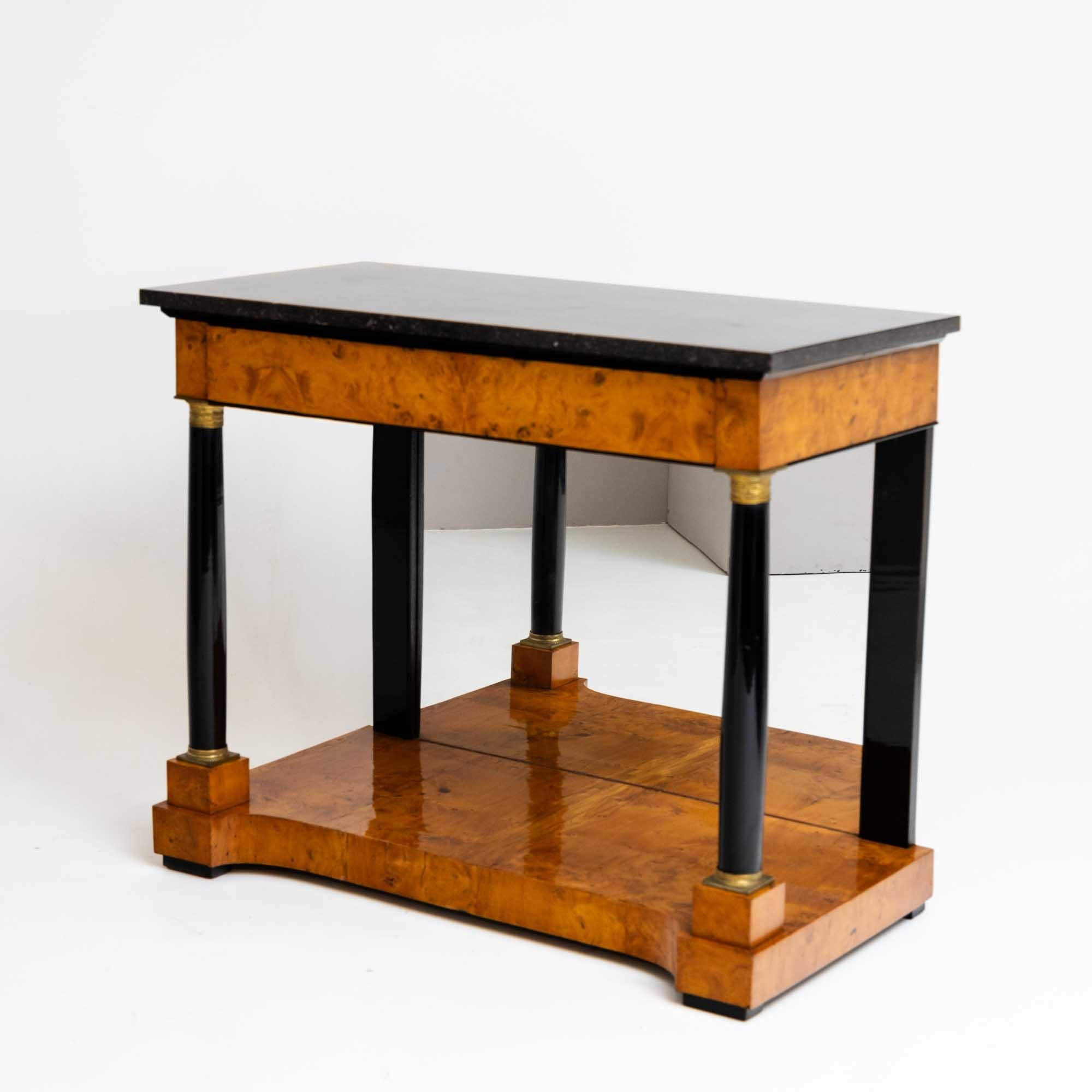 Elegant Biedermeier console table with dark granite top and mirrored back panel. The chest of drawers is veneered in burr walnut. The smooth frame is fitted with a drawer, which rests on ebonized columns with brass capitals and bases and pilasters