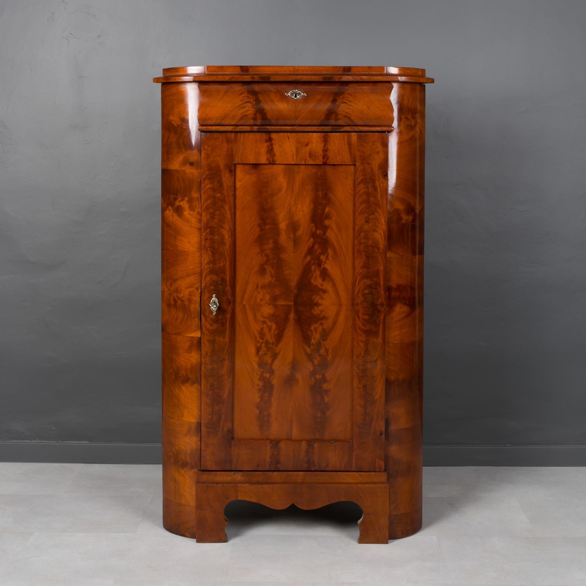 Biedermeier corner cabinet from 19th century. It comes from France most probably. It is made of pine wood, veneered with beautiful pyramidal mahogany. It features two shelves and a drawer, lockable with a key. It has undergone a careful renovation