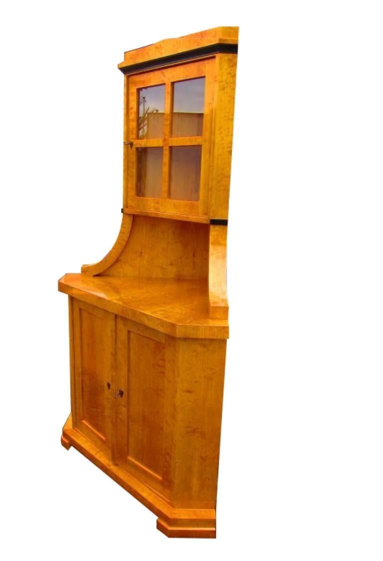 A Biedermeier corner cupboard from circa 1830. The body is made of softwood with a birchwood veneer. The birchwood creates a wonderful golden-brown color tone, and has a unique veneer grain. The top part has a door with four windows installed in